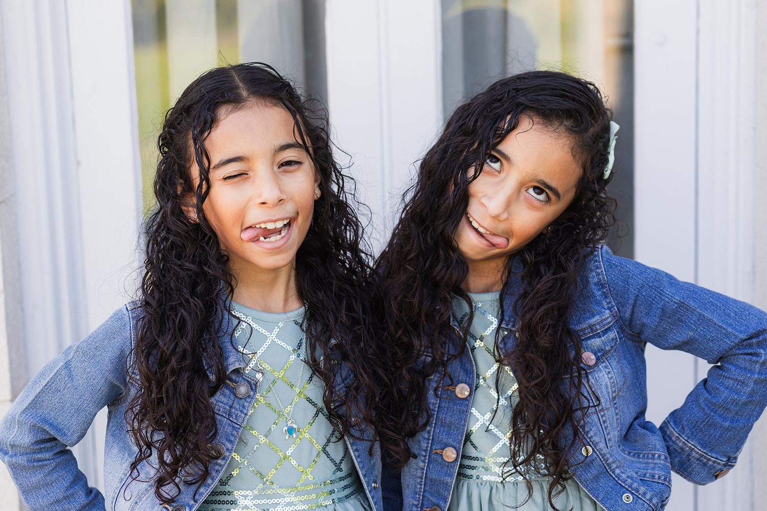 Two figures in matching outfits pose together against a white background with ferns.
