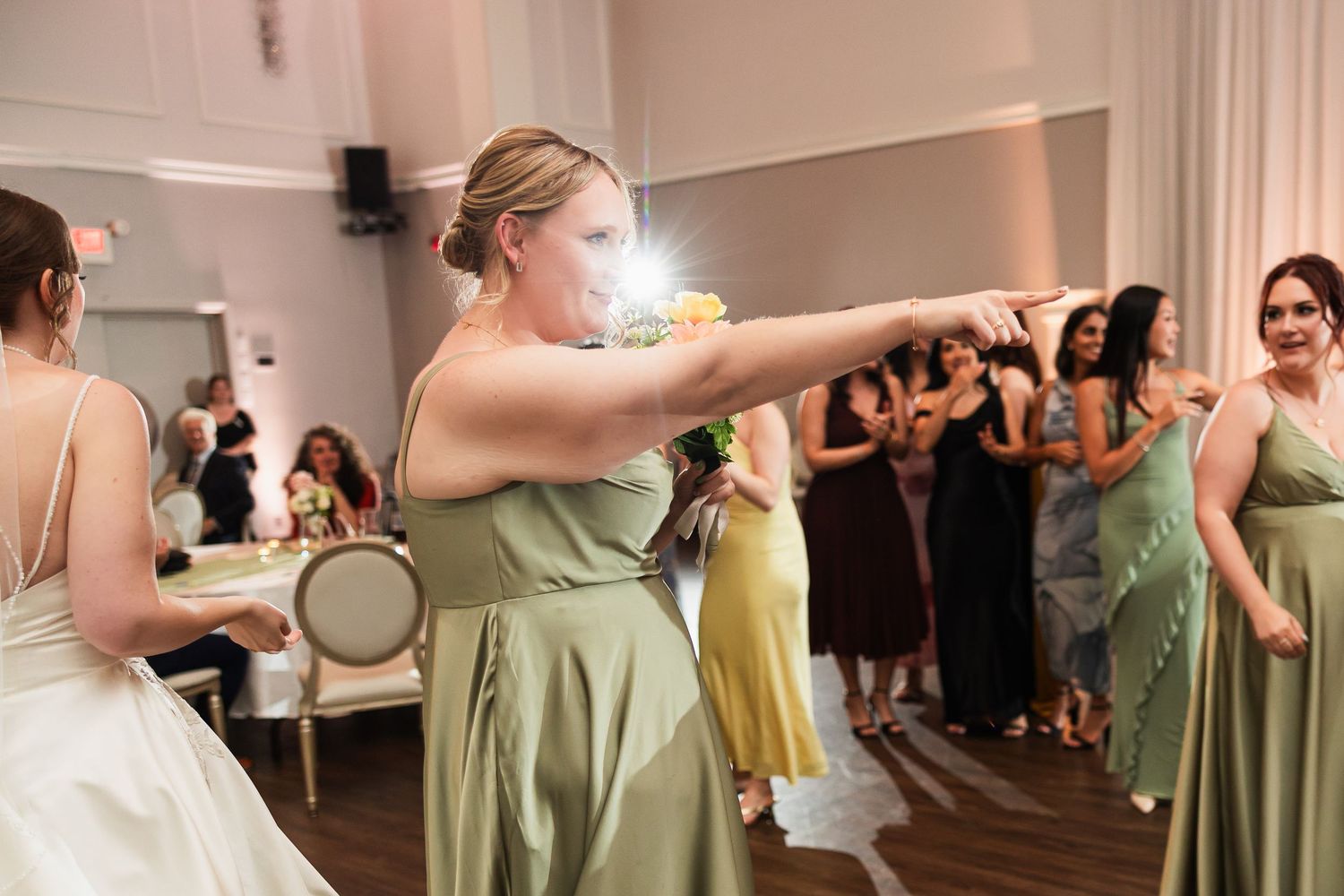 Bridesmaid in sage green dress tosses bouquet at elegant wedding reception.
