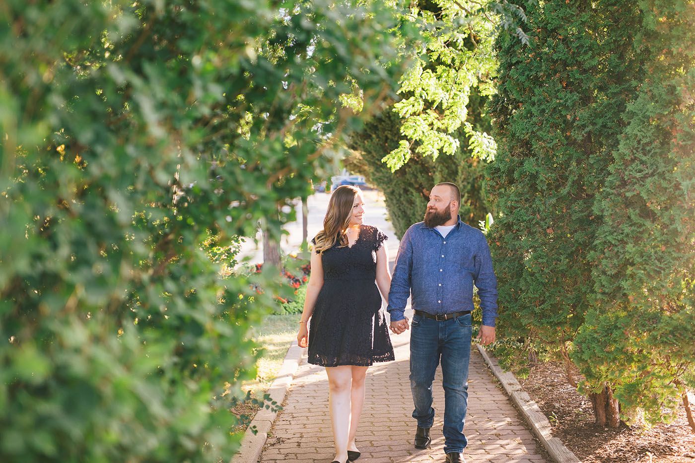 A couple walks together on a tree-lined path during an engagement photo session.