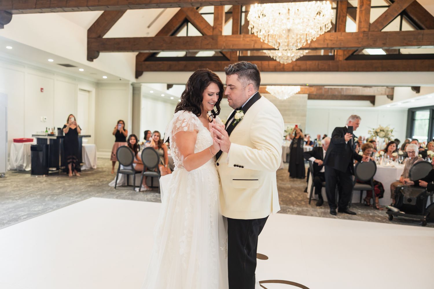 Bride and groom share their first dance on a white dance floor at elegant wedding reception.