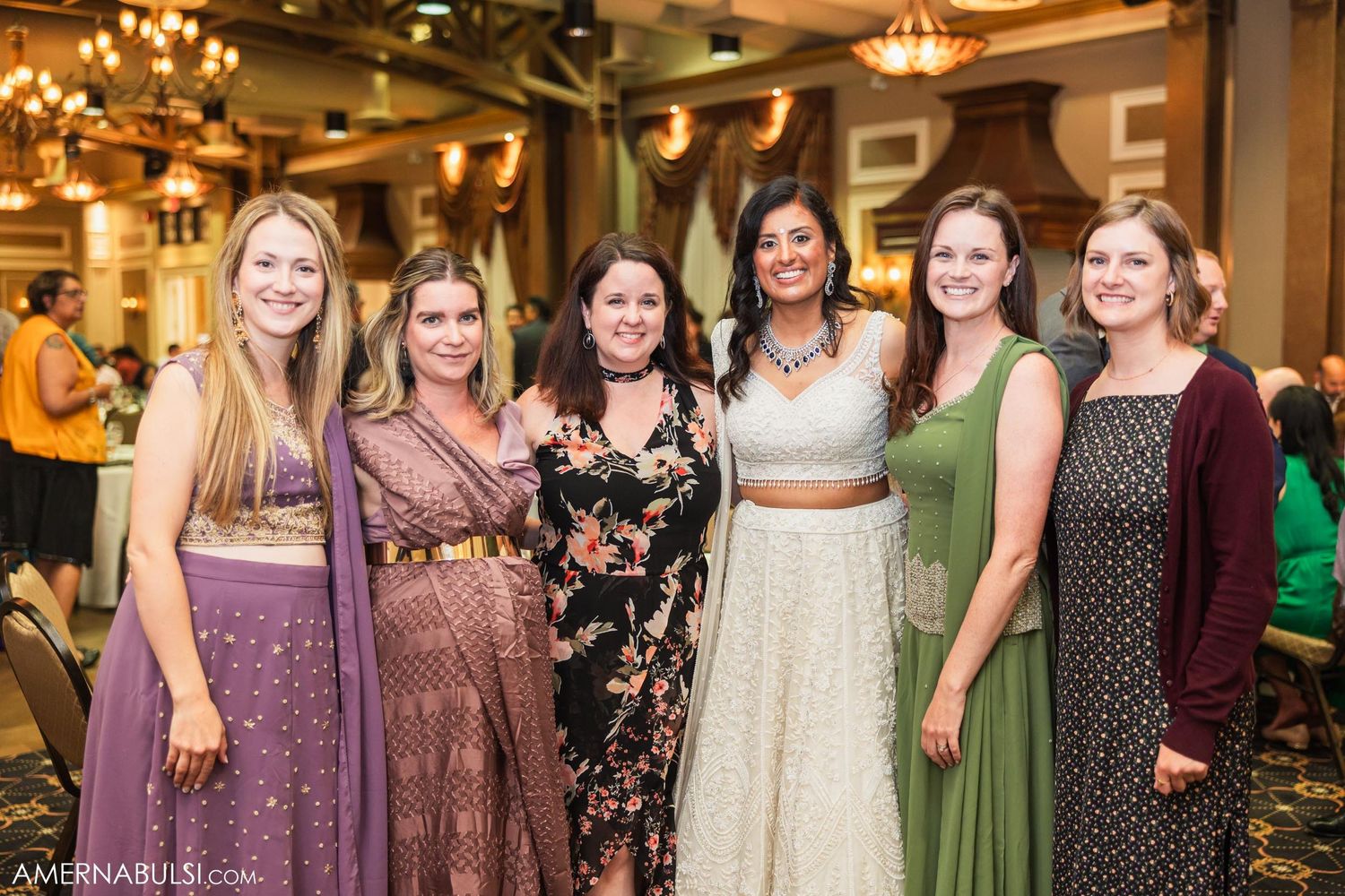 Wedding guests in colorful formal attire pose together at an indoor reception venue.