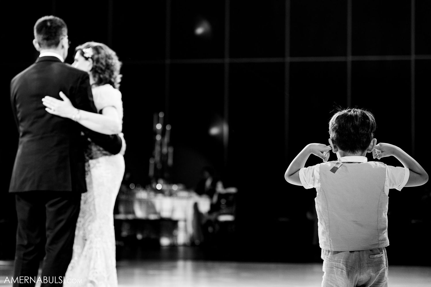 A couple dances while a small child watches and mimics their moves in a black and white photo.