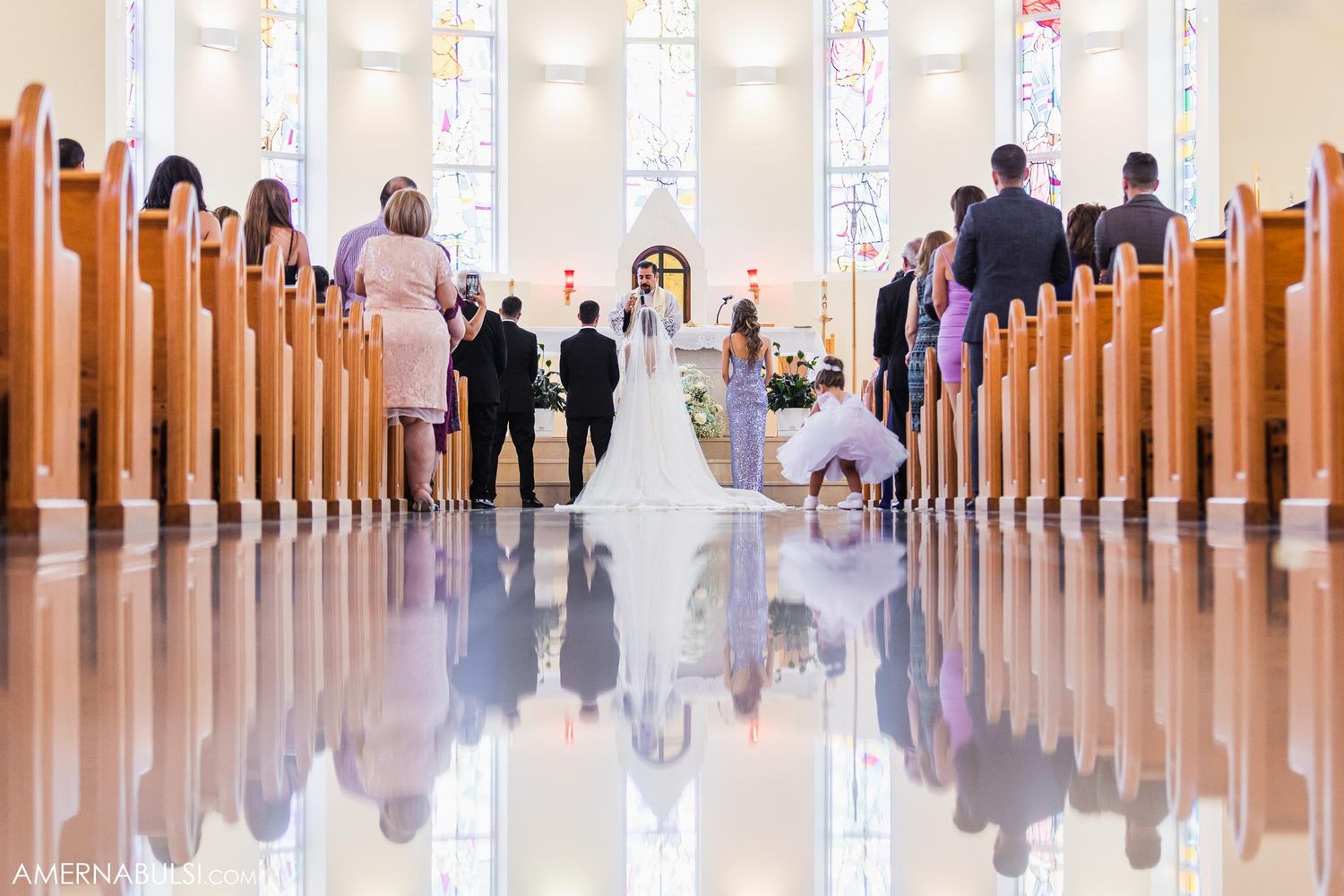 Church interior with reflective floor shows wedding ceremony from rear view perspective.