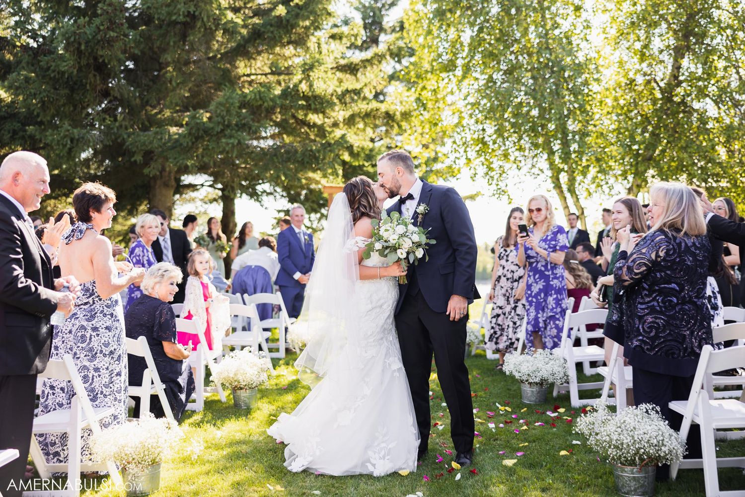 Newlyweds share their first kiss as guests celebrate during an outdoor garden wedding ceremony.