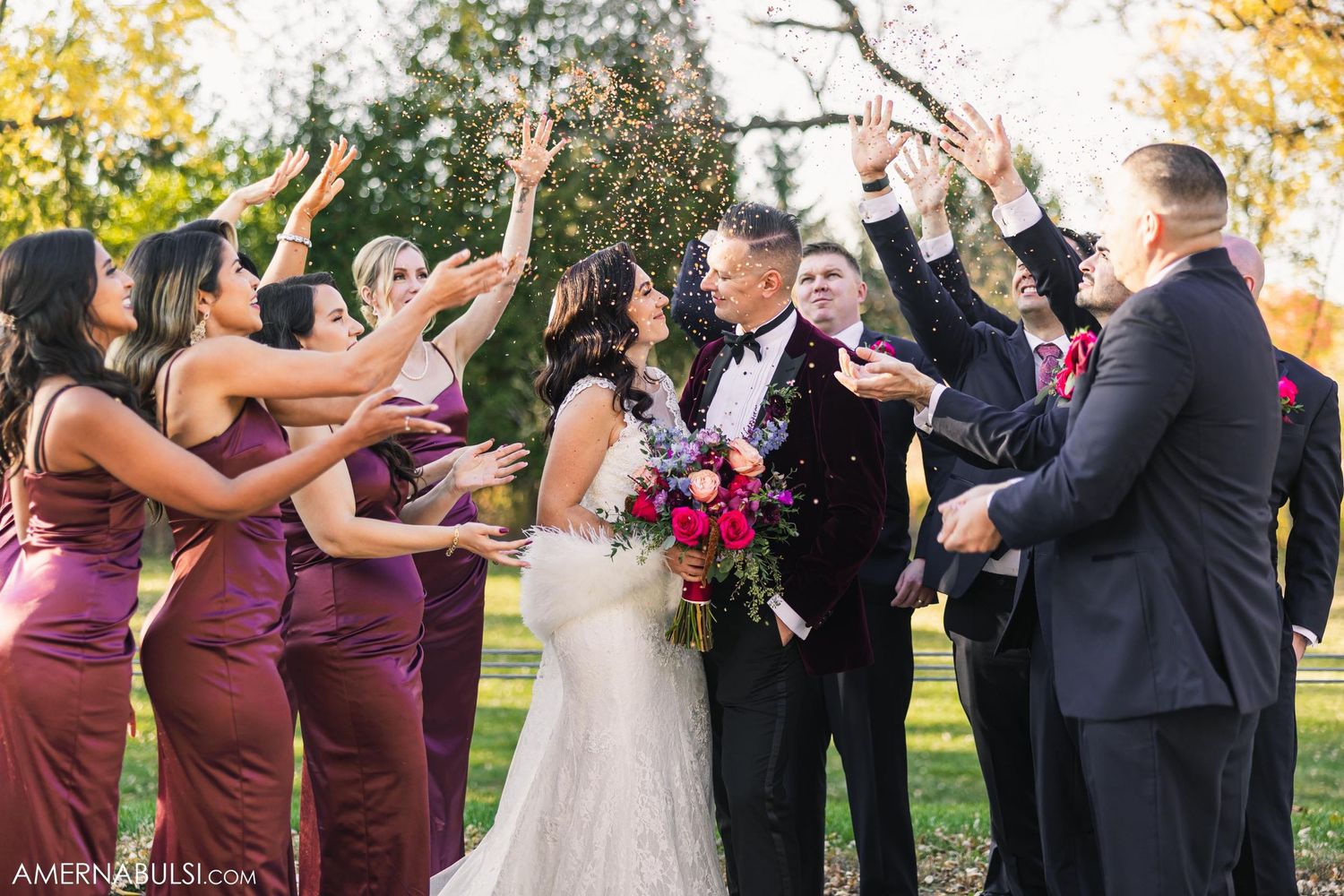 Wedding party celebrating with raised hands outdoors in autumn setting.