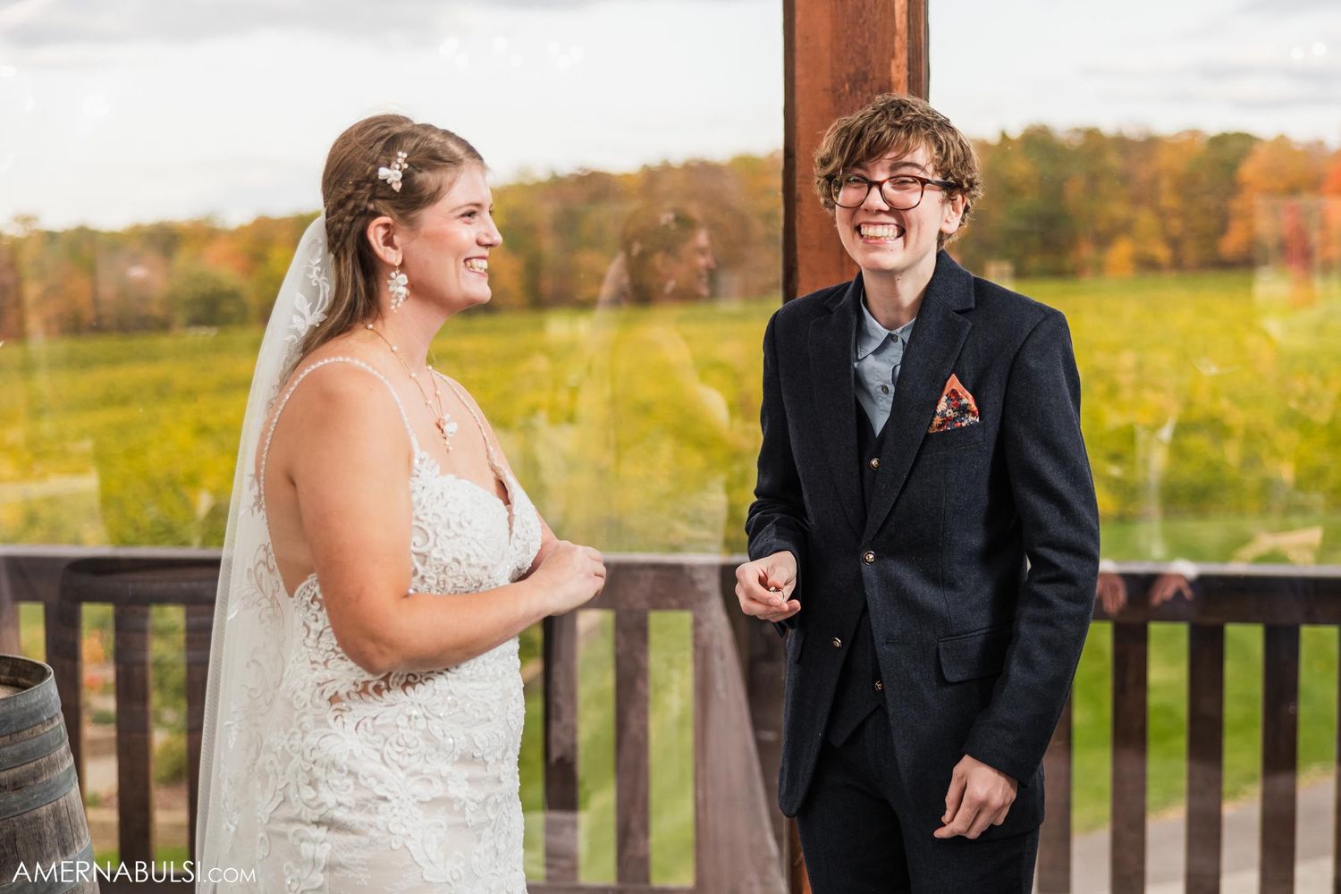 A wedding couple exchanges vows on an outdoor deck with autumn scenery in the background.