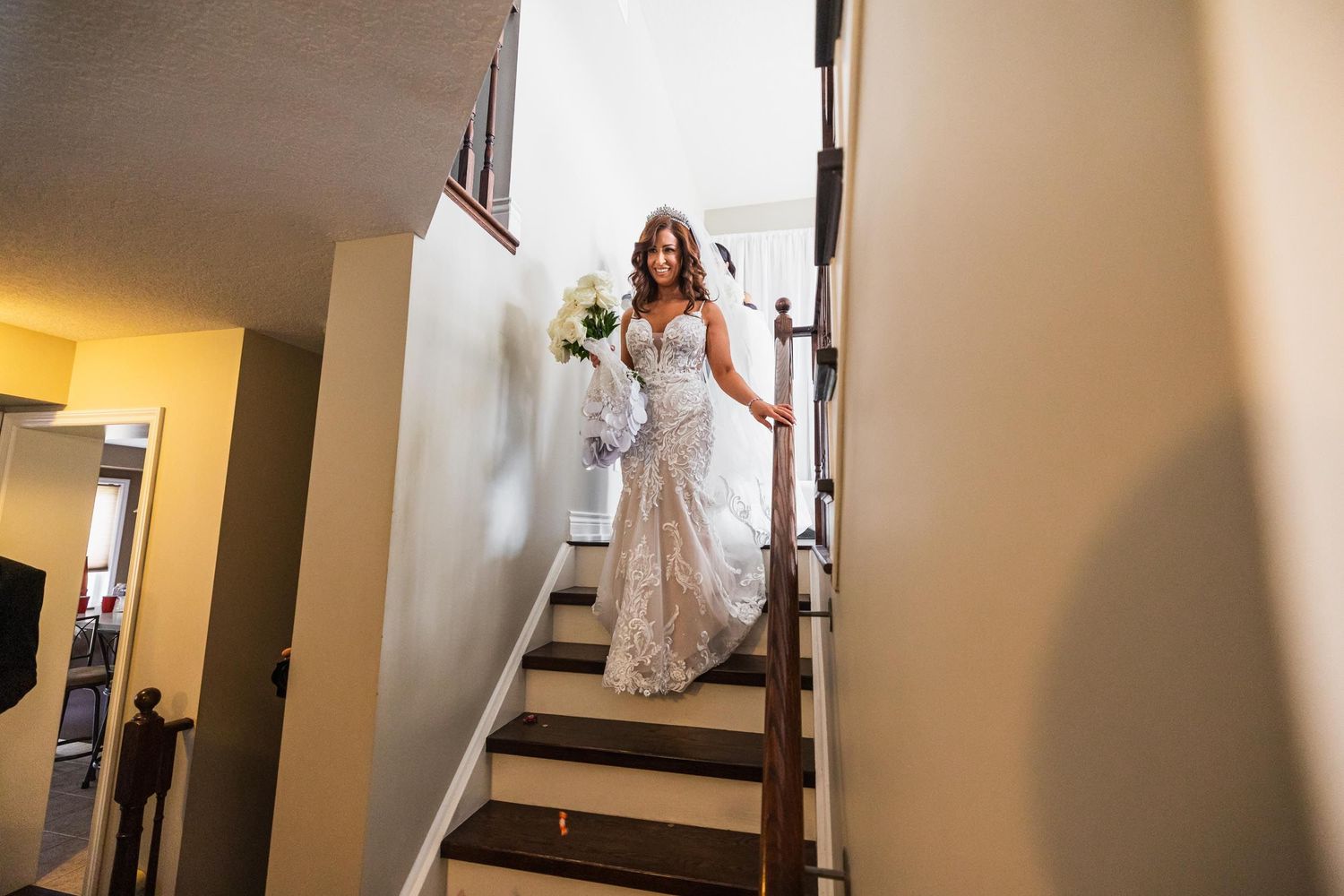 A bride in an ornate lace gown walks down interior stairs.