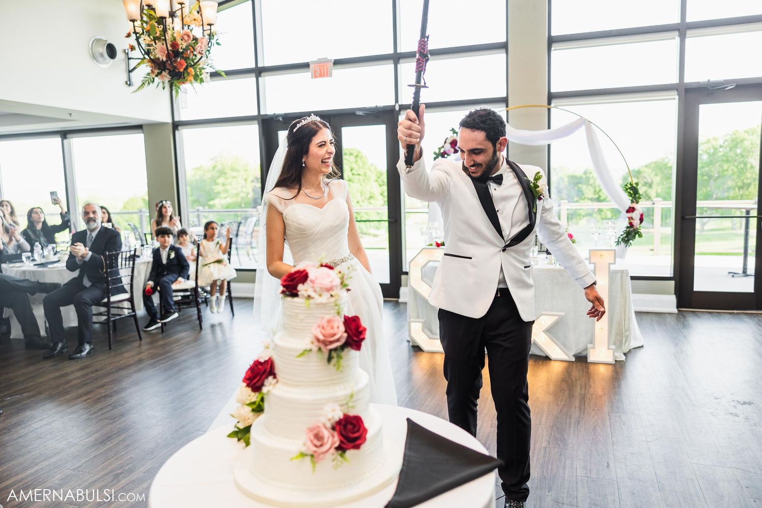 Couple cutting their elegant white and pink floral wedding cake in bright reception venue.