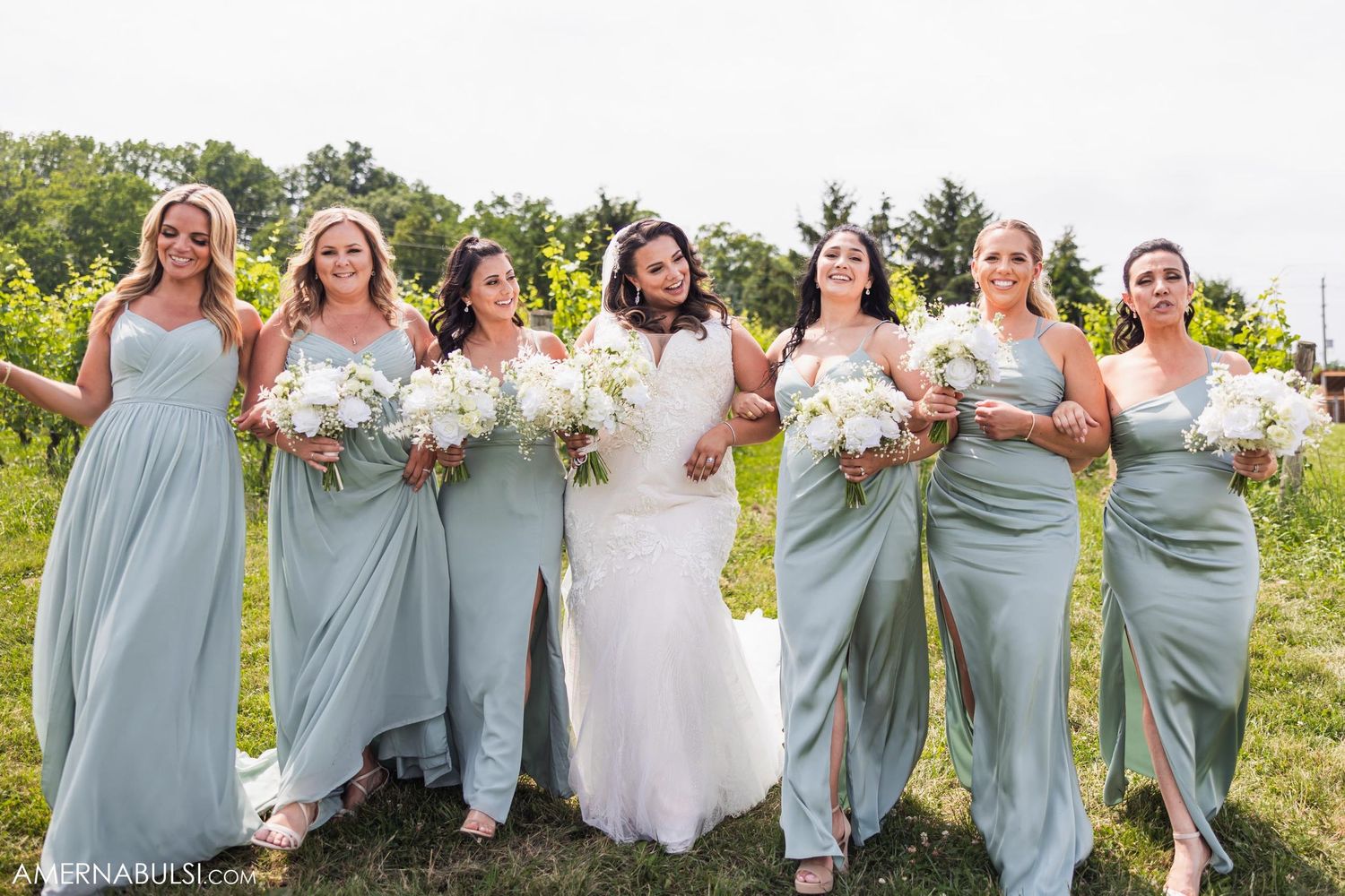 Wedding party with bridesmaids in matching sage dresses holding white flower bouquets.