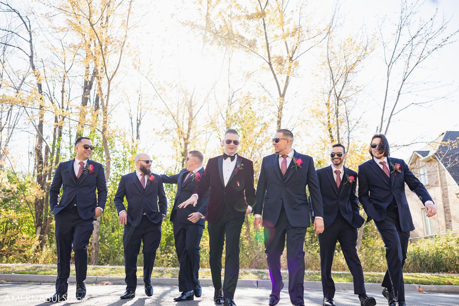 Groomsmen in dark suits walking together on sunny autumn path.