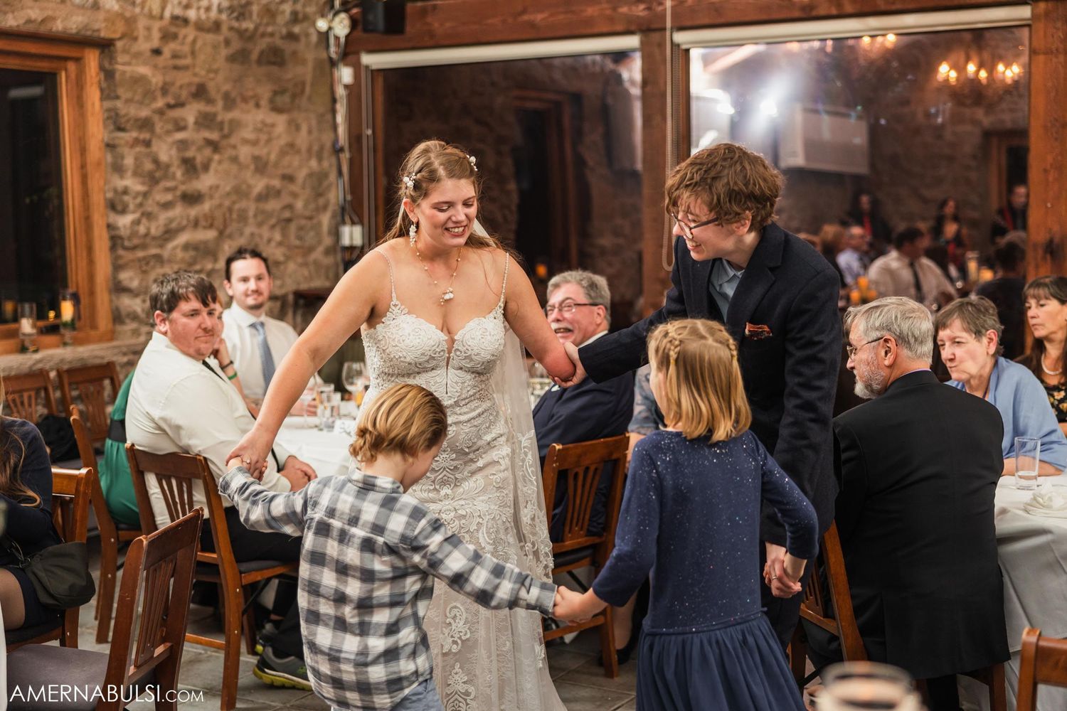 Wedding reception dance with young guests joining in at rustic stone venue.