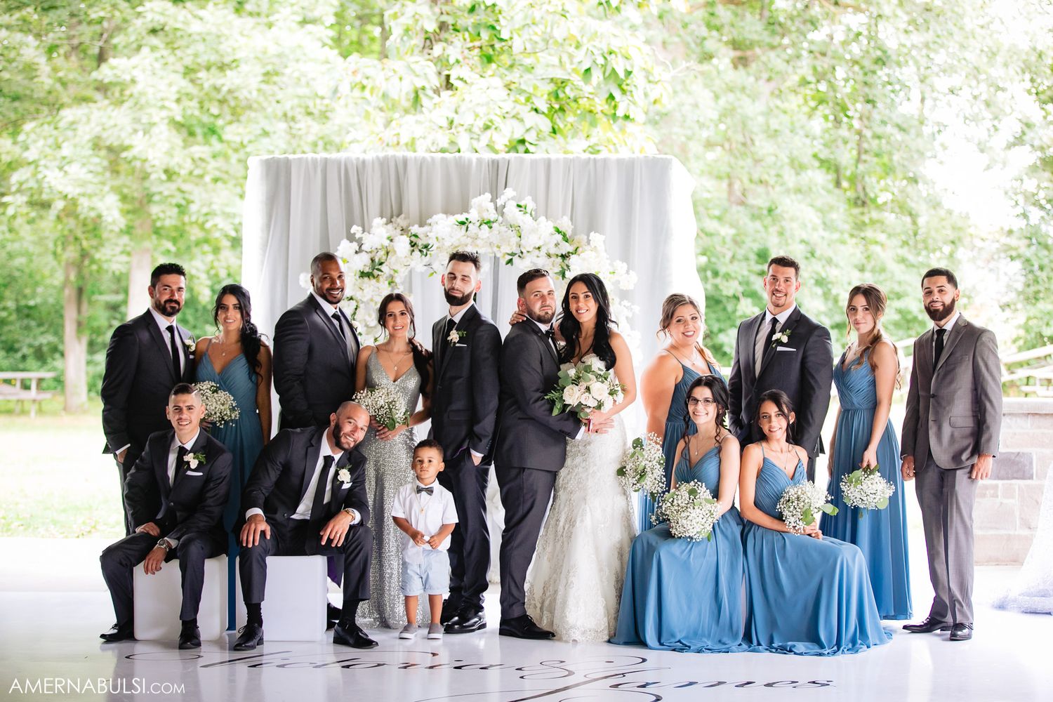Wedding party lined up outdoors wearing blue and black formal attire.