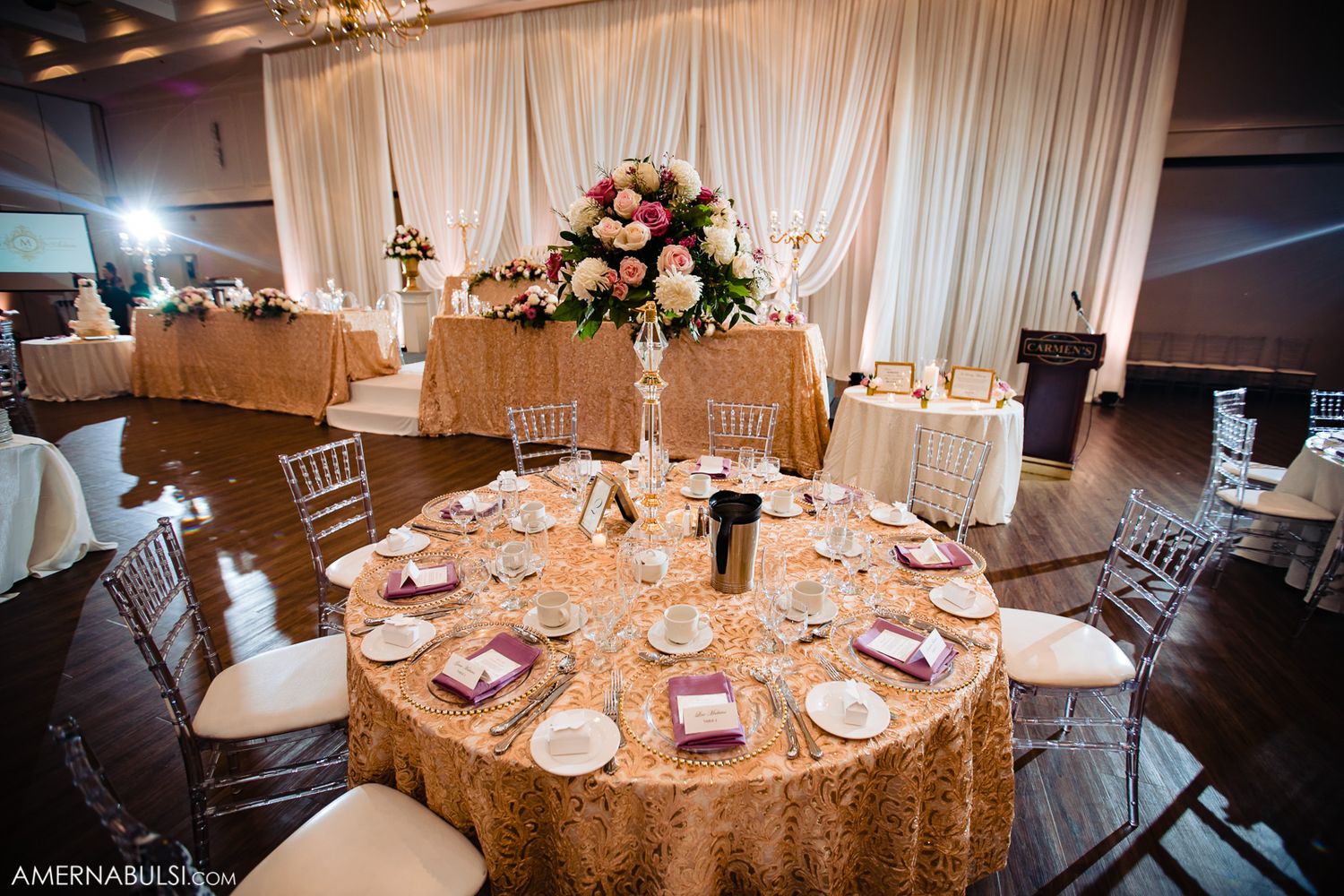 Elegant wedding reception table with gold sequin tablecloth and floral centerpiece against white draped backdrop.