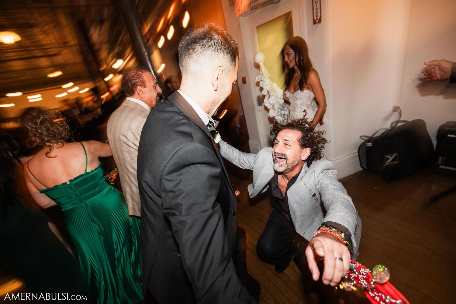 Wedding guests dancing energetically on the dance floor at a reception with warm lighting.