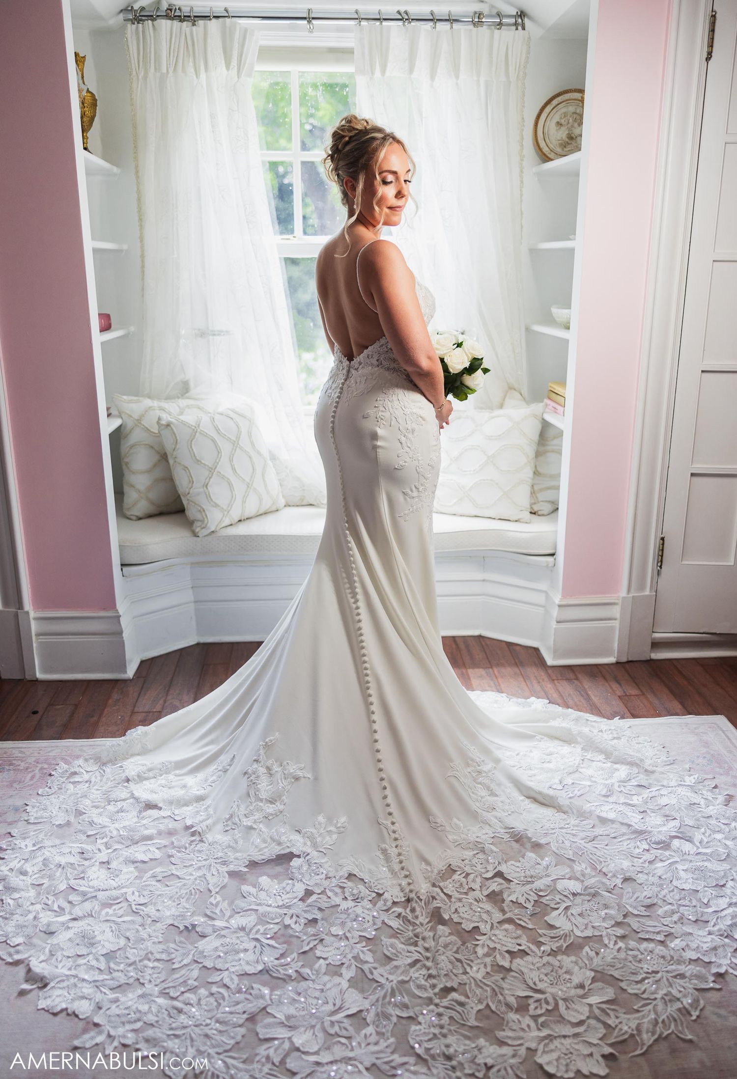 Elegant white lace wedding gown with open back and long train displayed in natural window light.