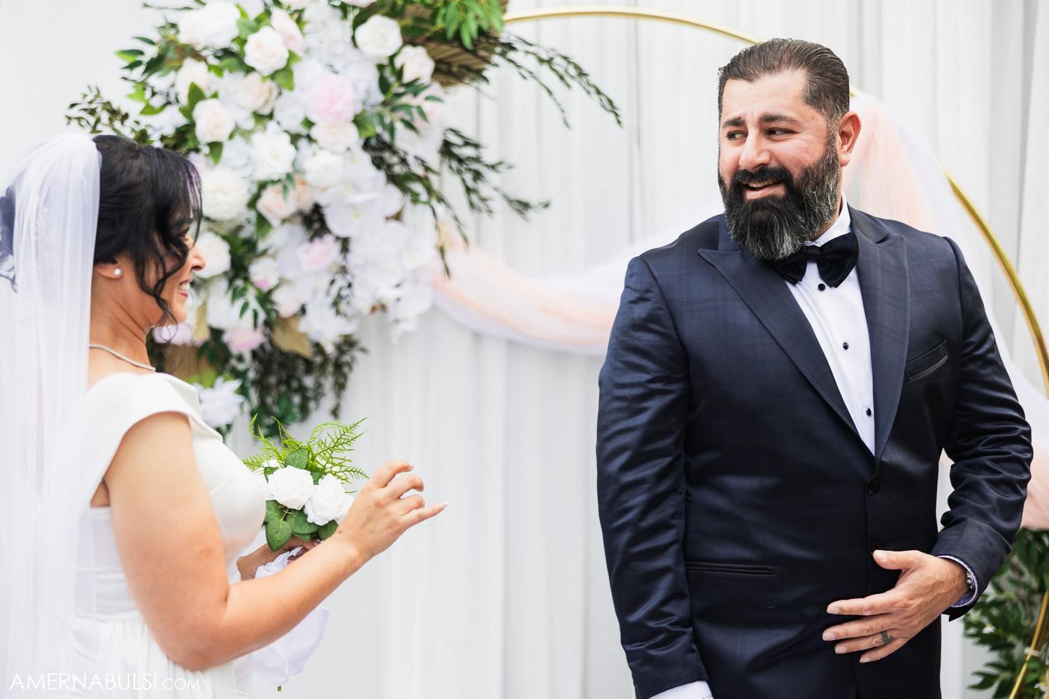 Happy couple exchanging vows during wedding ceremony with elegant white flower backdrop.