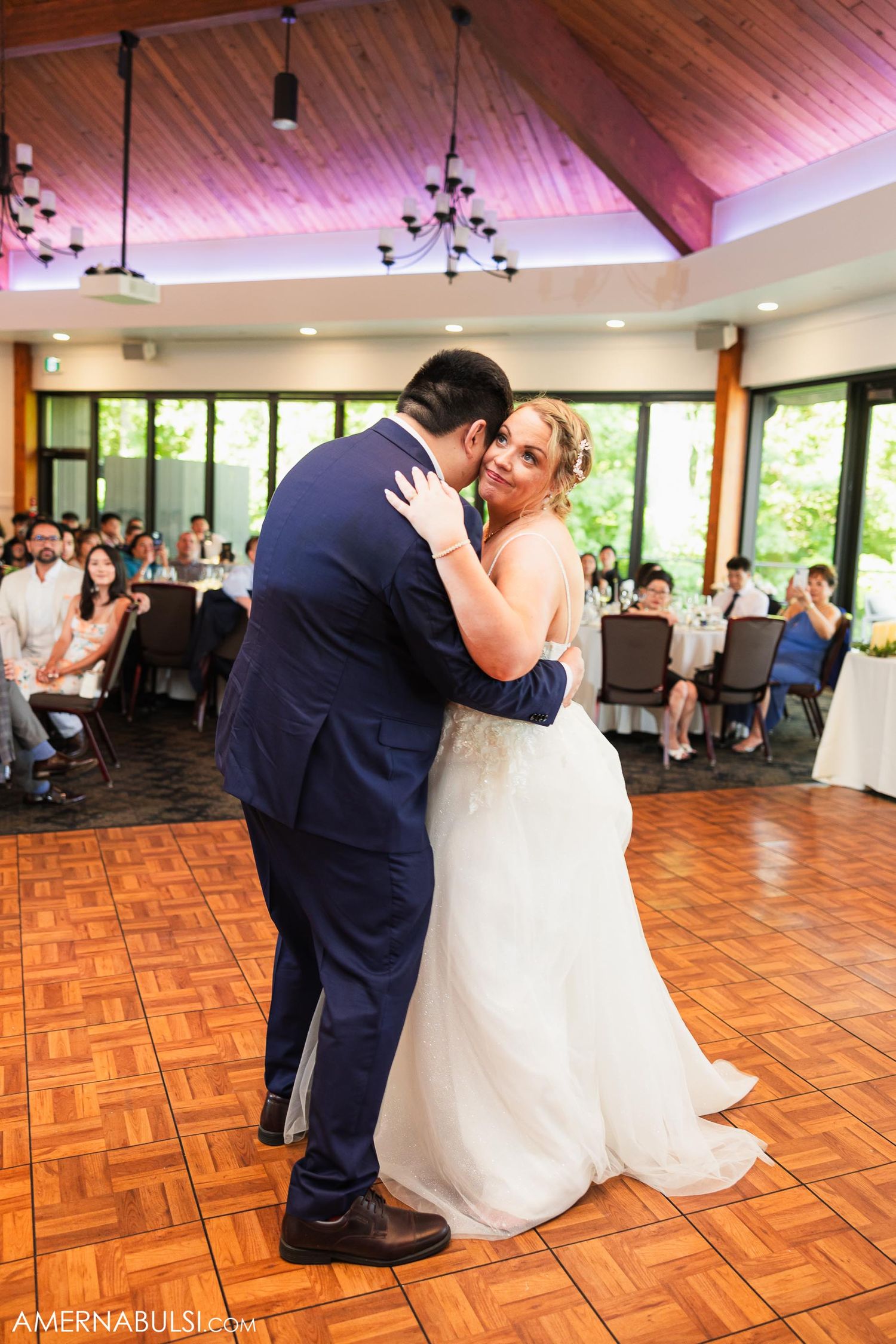 Newlyweds share their first dance on parquet floor at wedding reception venue.