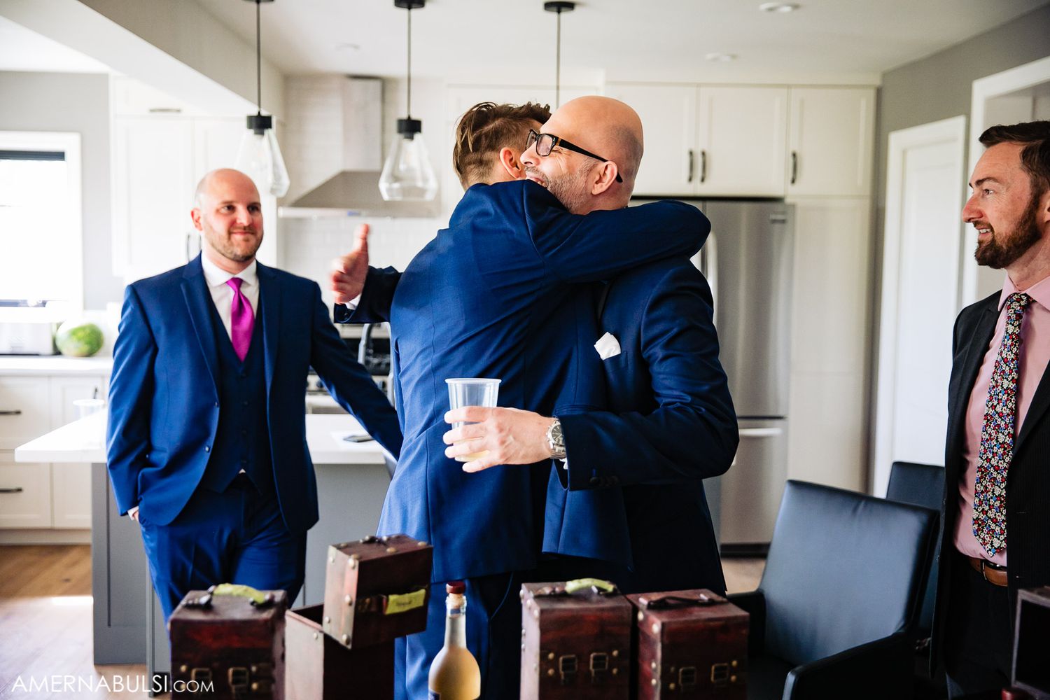 Group of men in navy suits gathered in a modern kitchen during wedding preparations.