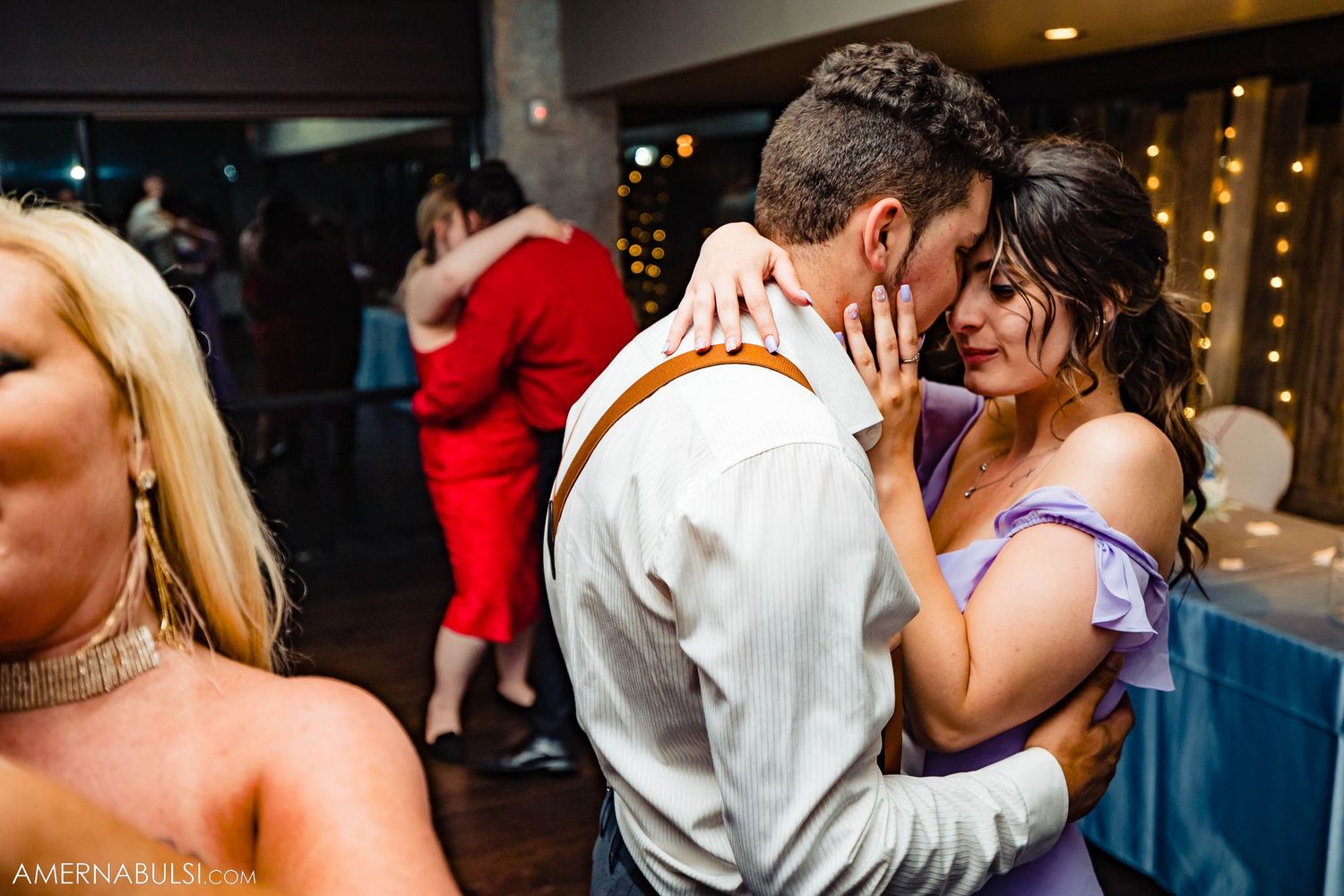 Intimate moment between dancers on crowded reception dance floor.