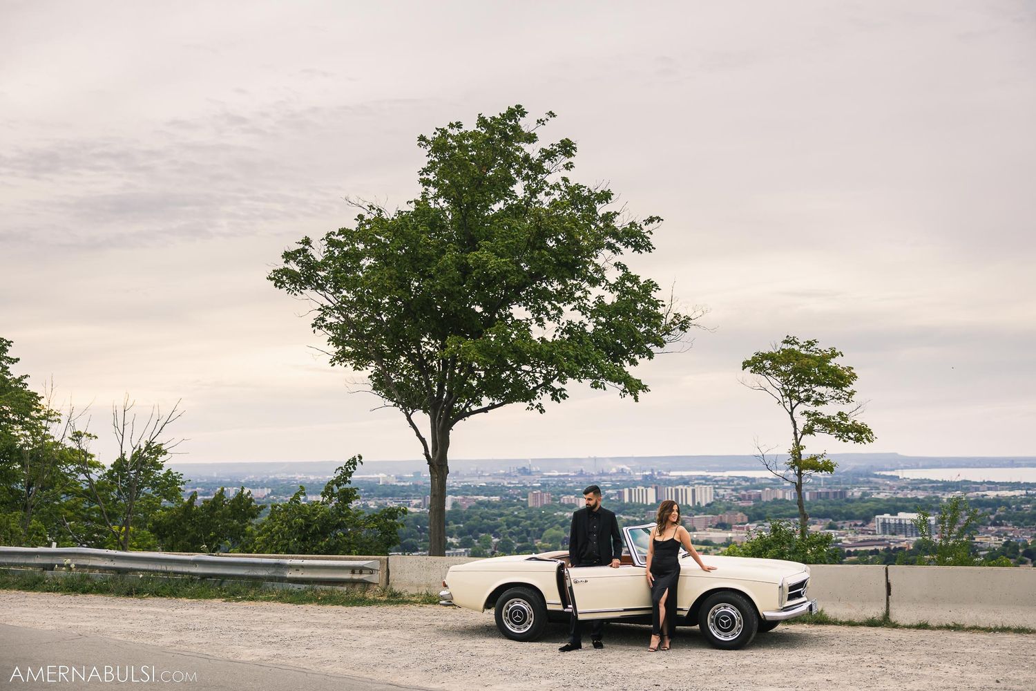 Scenic overlook featuring a vintage white Mercedes-Benz and expansive city views.