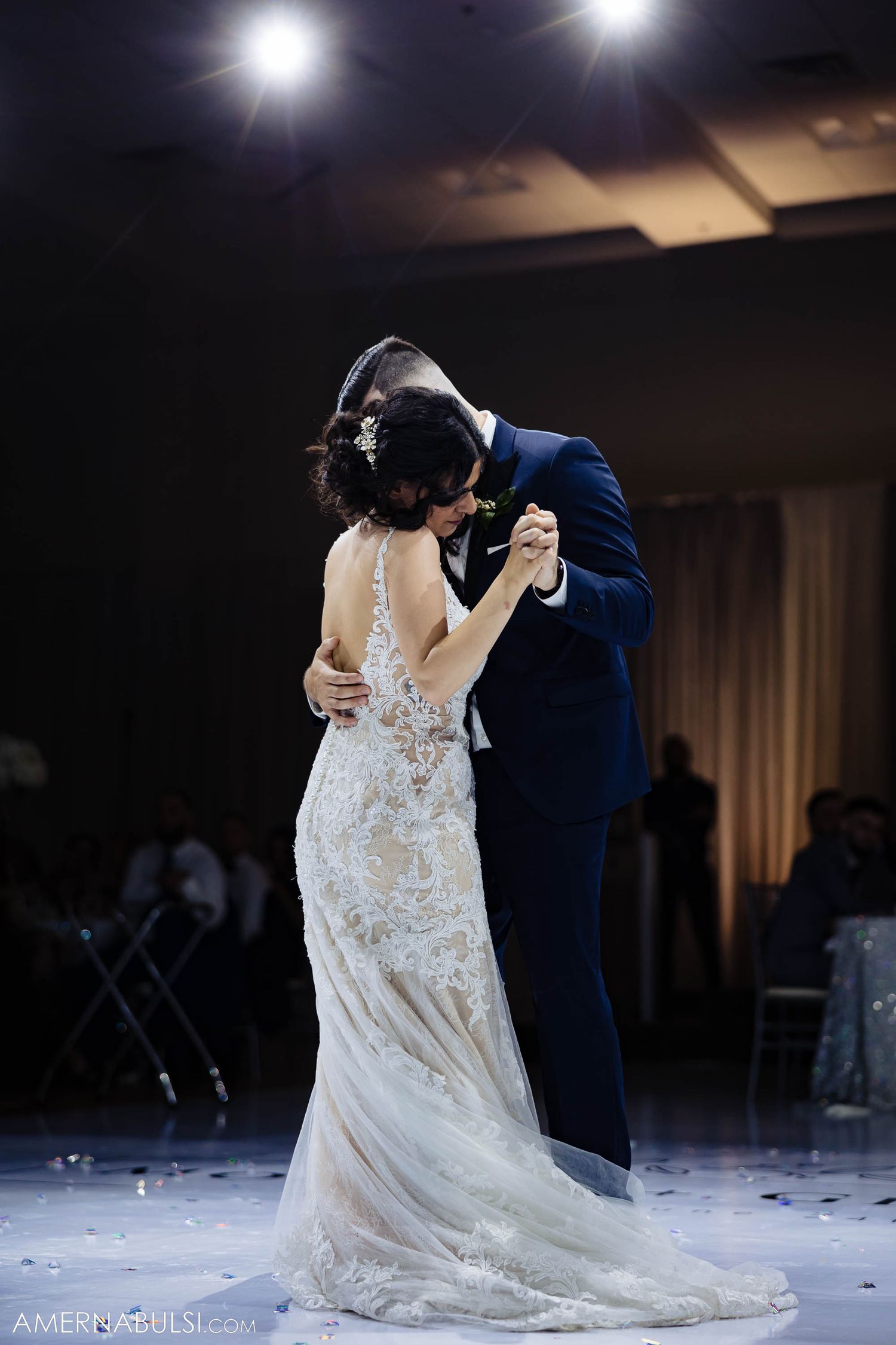 Intimate wedding dance captured under dramatic spotlight with bride's lace dress trailing beautifully.