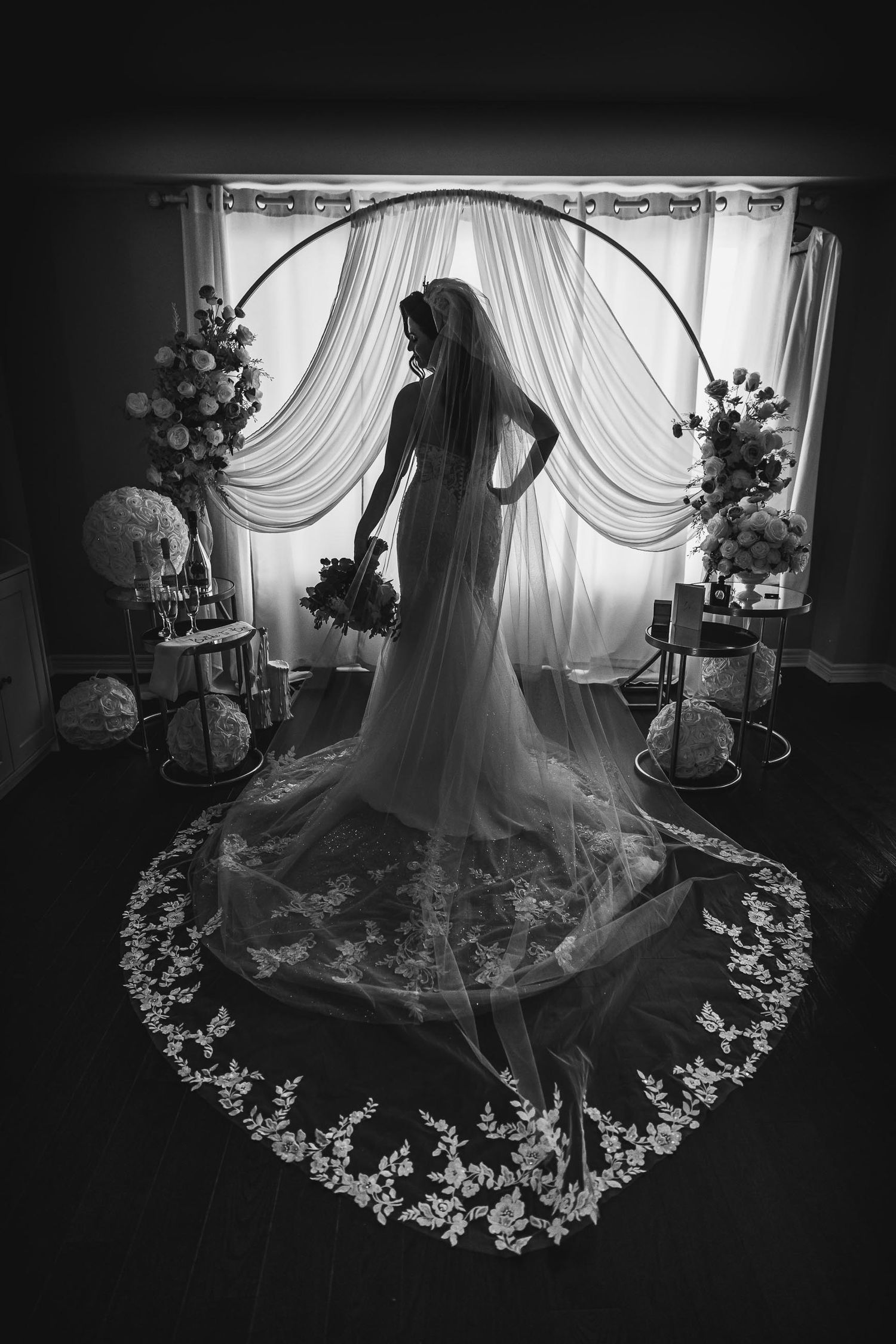 A silhouette stands before a draped arch with flowing veil creating heart-shaped lace pattern.