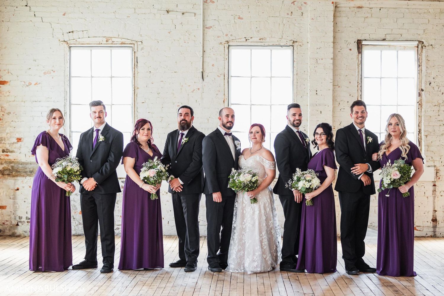 Wedding party lined up in industrial venue with purple bridesmaid dresses.