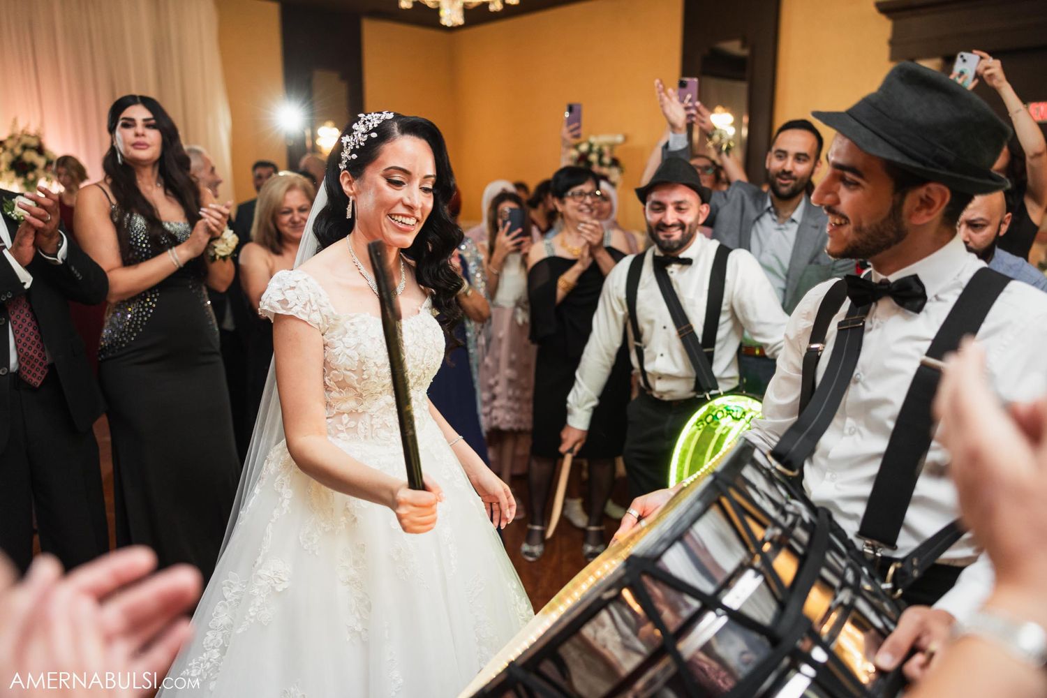 Musicians in suspenders perform while wedding guests dance and celebrate in a banquet hall.