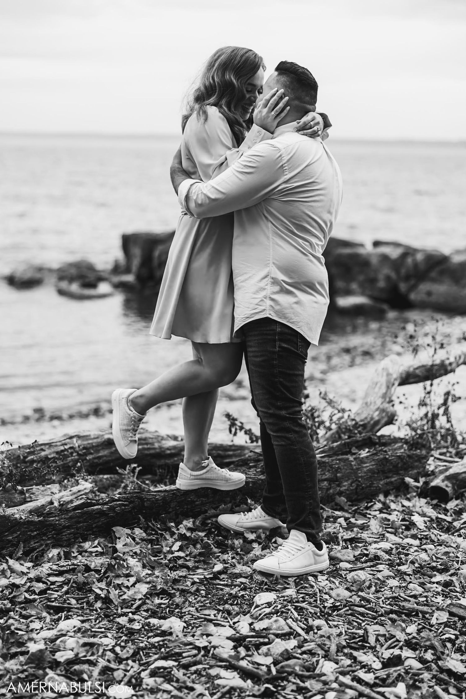 A romantic moment captured between a couple on a rocky beach shoreline.