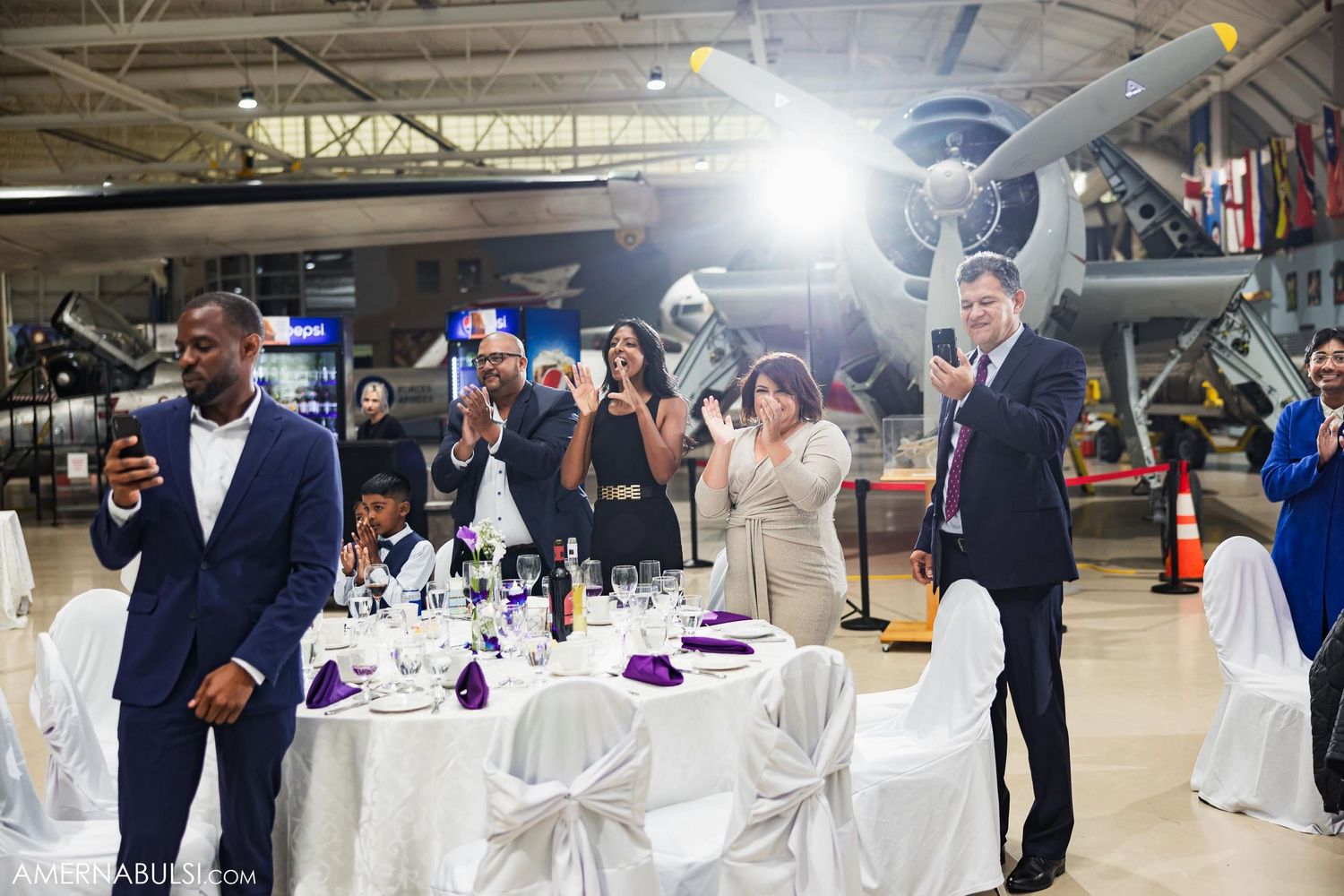 Wedding guests in formal attire toast and celebrate at an aviation-themed reception venue.