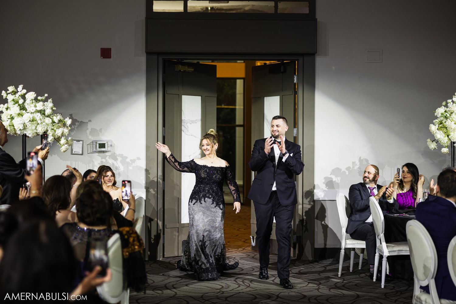 A couple makes their grand entrance through doorways as wedding guests applaud their arrival.