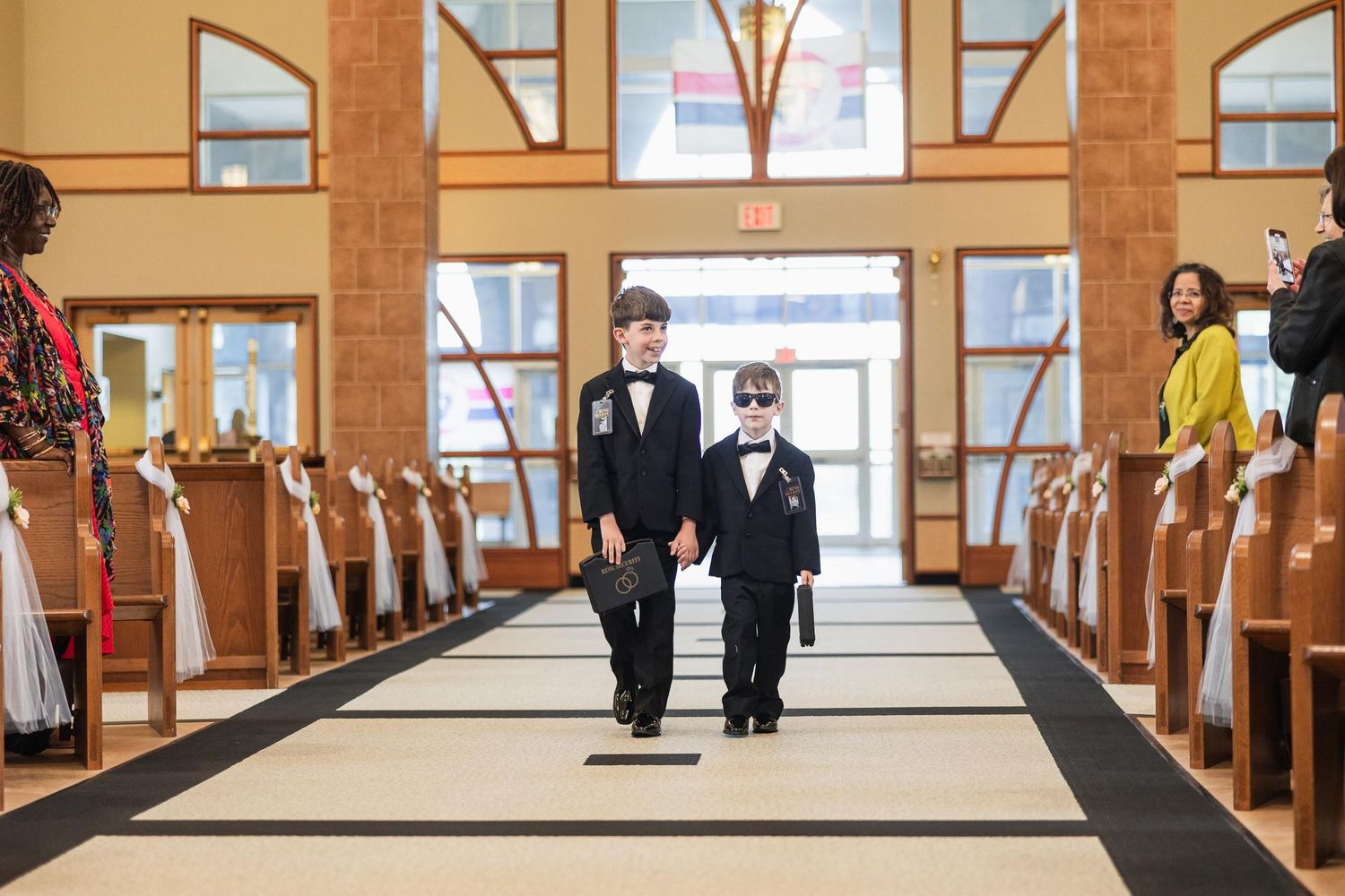 Two people in formal attire walking down the center aisle of a church.