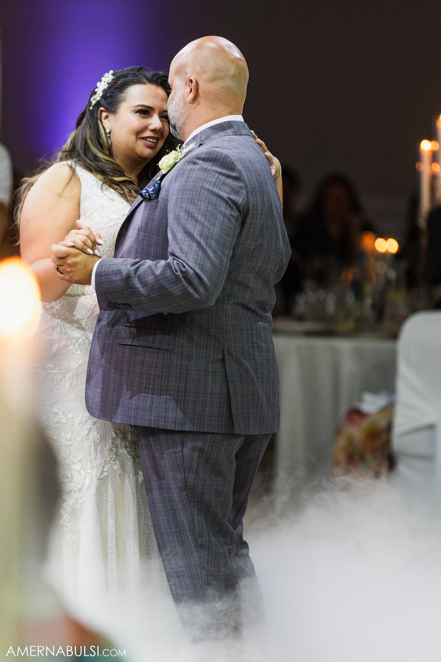 Intimate wedding dance moment captured through glowing candlelight with fog effect on dancefloor.
