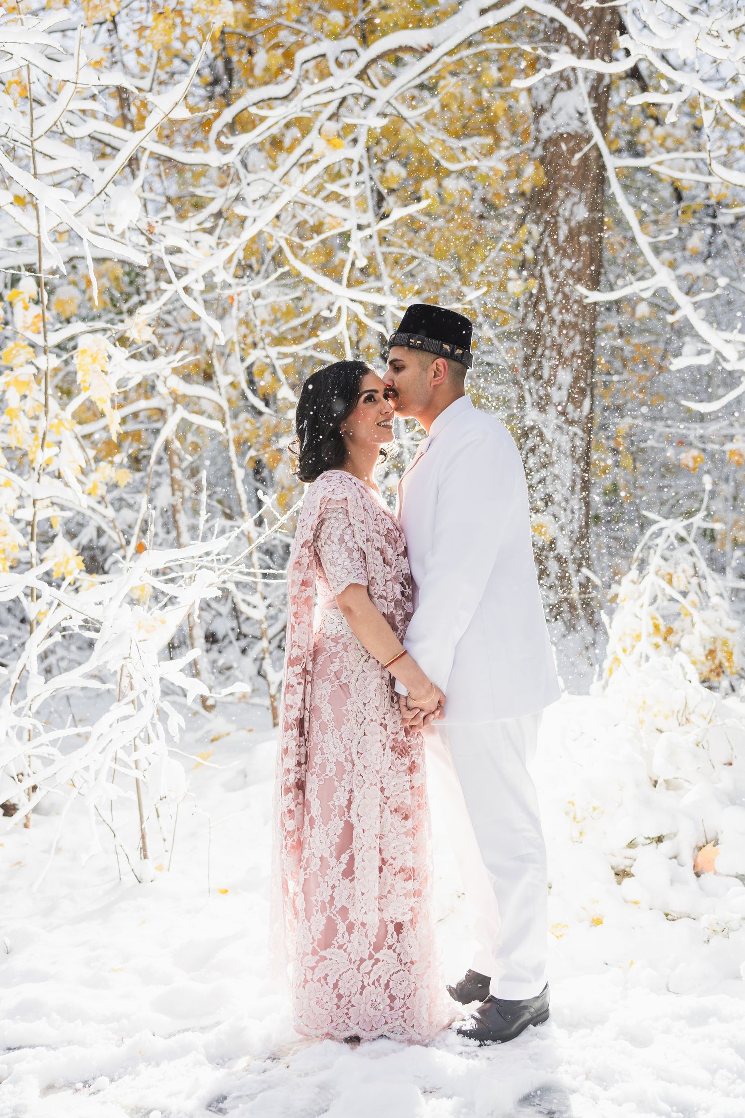 Couple poses together in snowy winter wonderland with snow-covered trees.