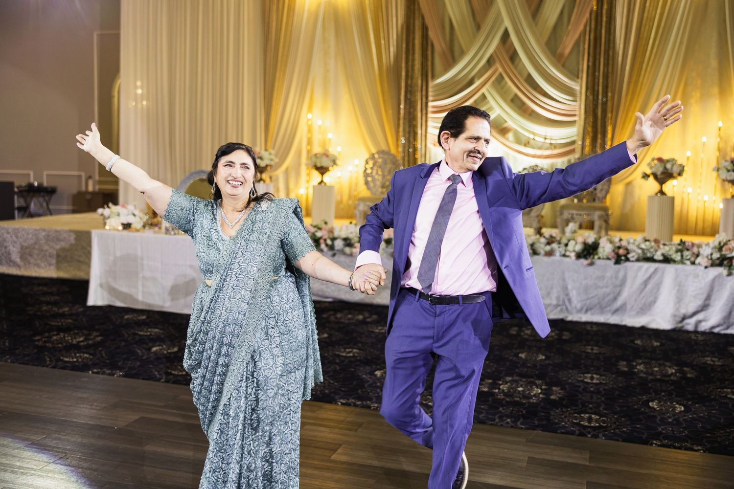 Dancers performing energetic moves in a ballroom with ornate gold curtains and chandeliers.