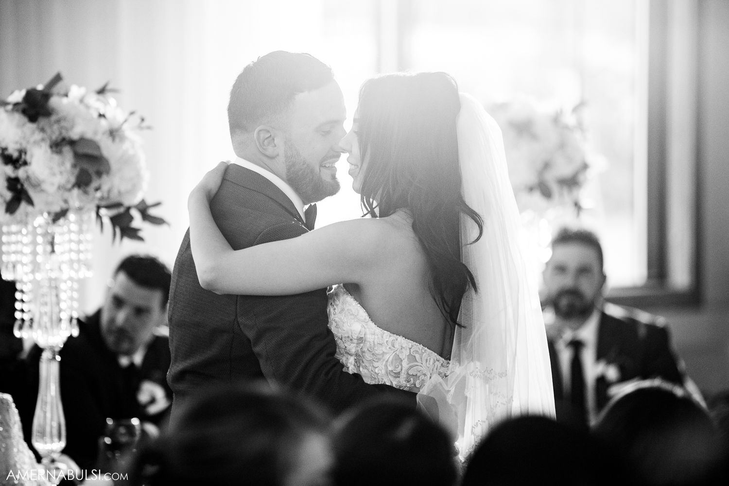 Black and white artistic wedding reception photo showing silhouettes against dramatic lighting.