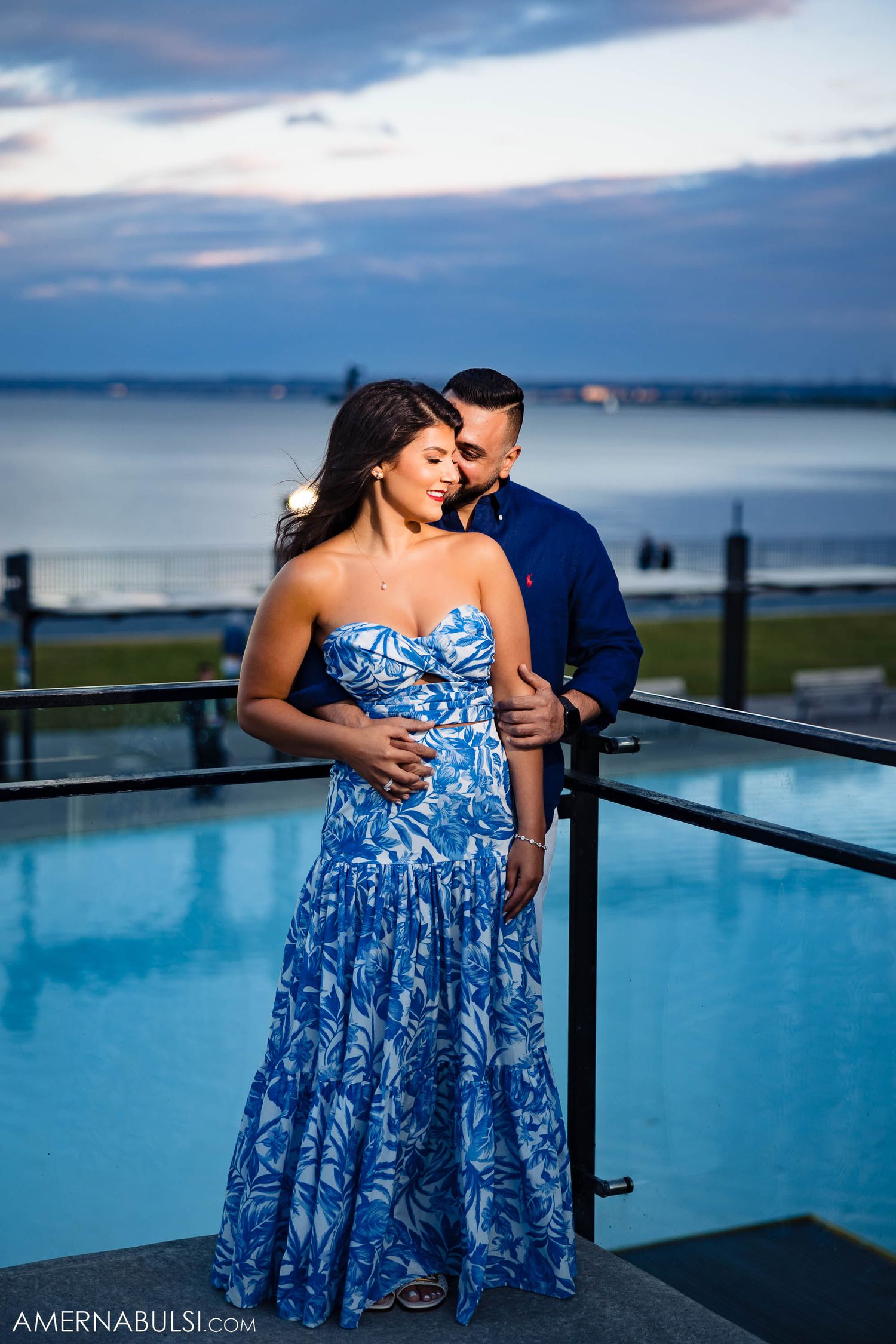 Couple sharing intimate moment by infinity pool with waterfront views at dusk.