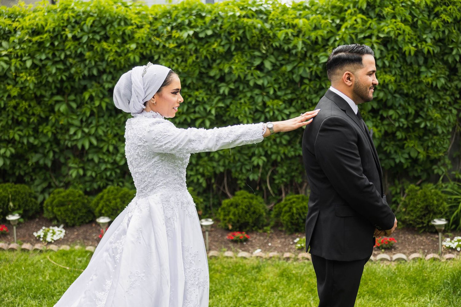 A first look moment between bride and groom with a green hedge backdrop in an outdoor garden setting.