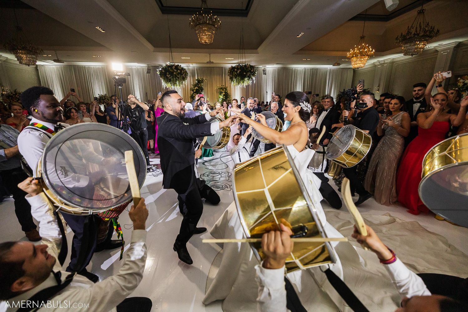 Energetic drummers entertaining wedding guests on a dance floor with dramatic lighting.