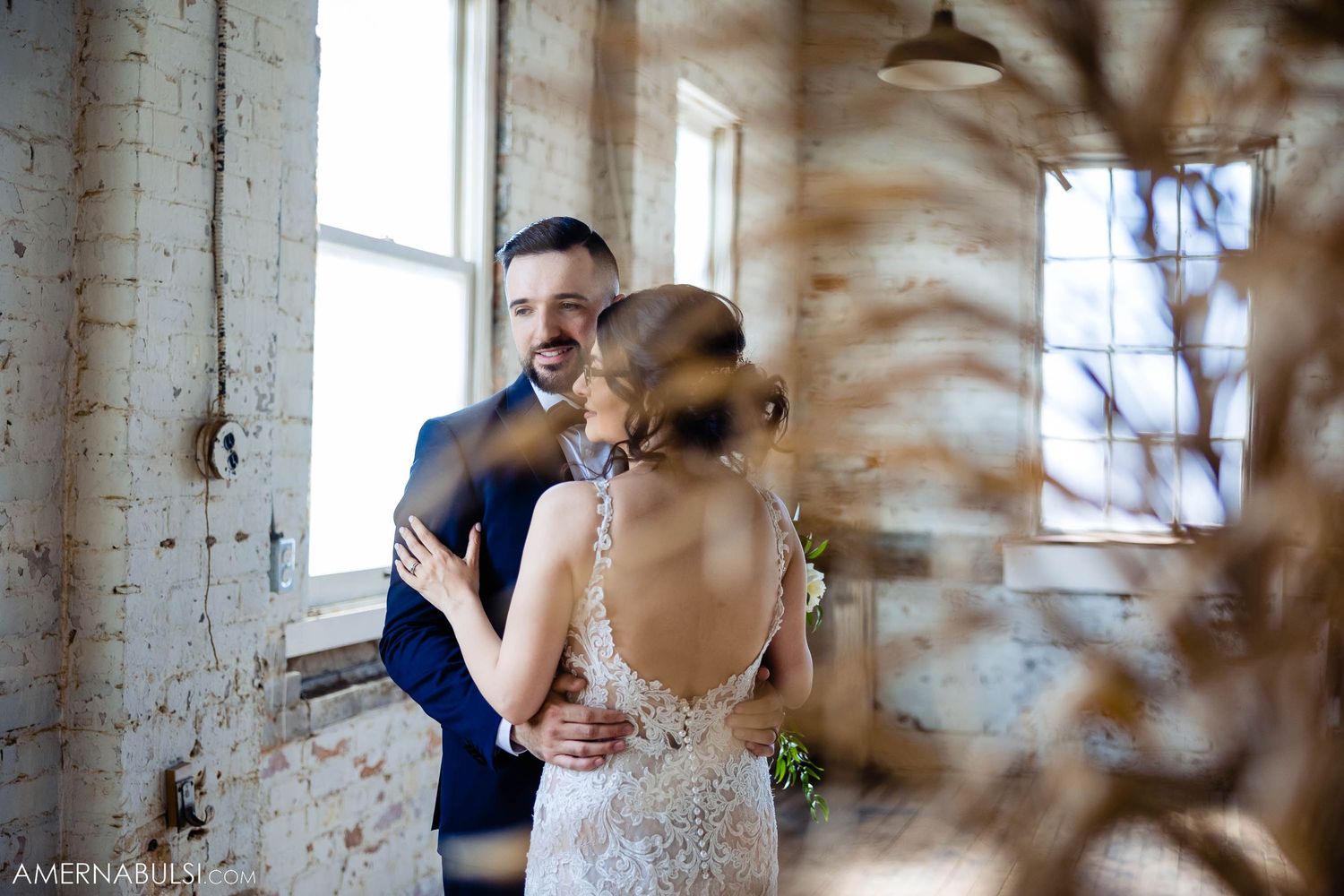 A tender moment between newlyweds as they embrace in an industrial-style venue with brick walls.