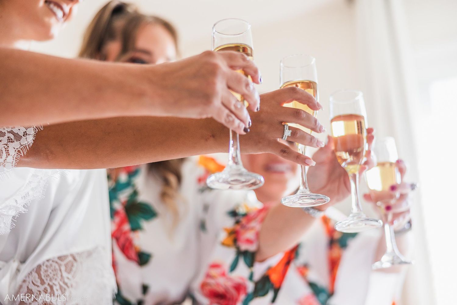 Close-up of hands clinking champagne glasses while wearing floral robes.