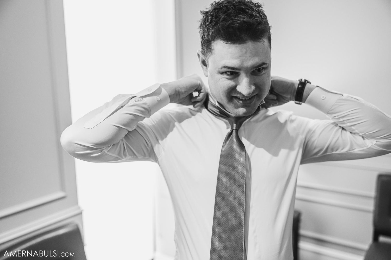 Black and white photo of person adjusting collar and tie during wedding preparations.