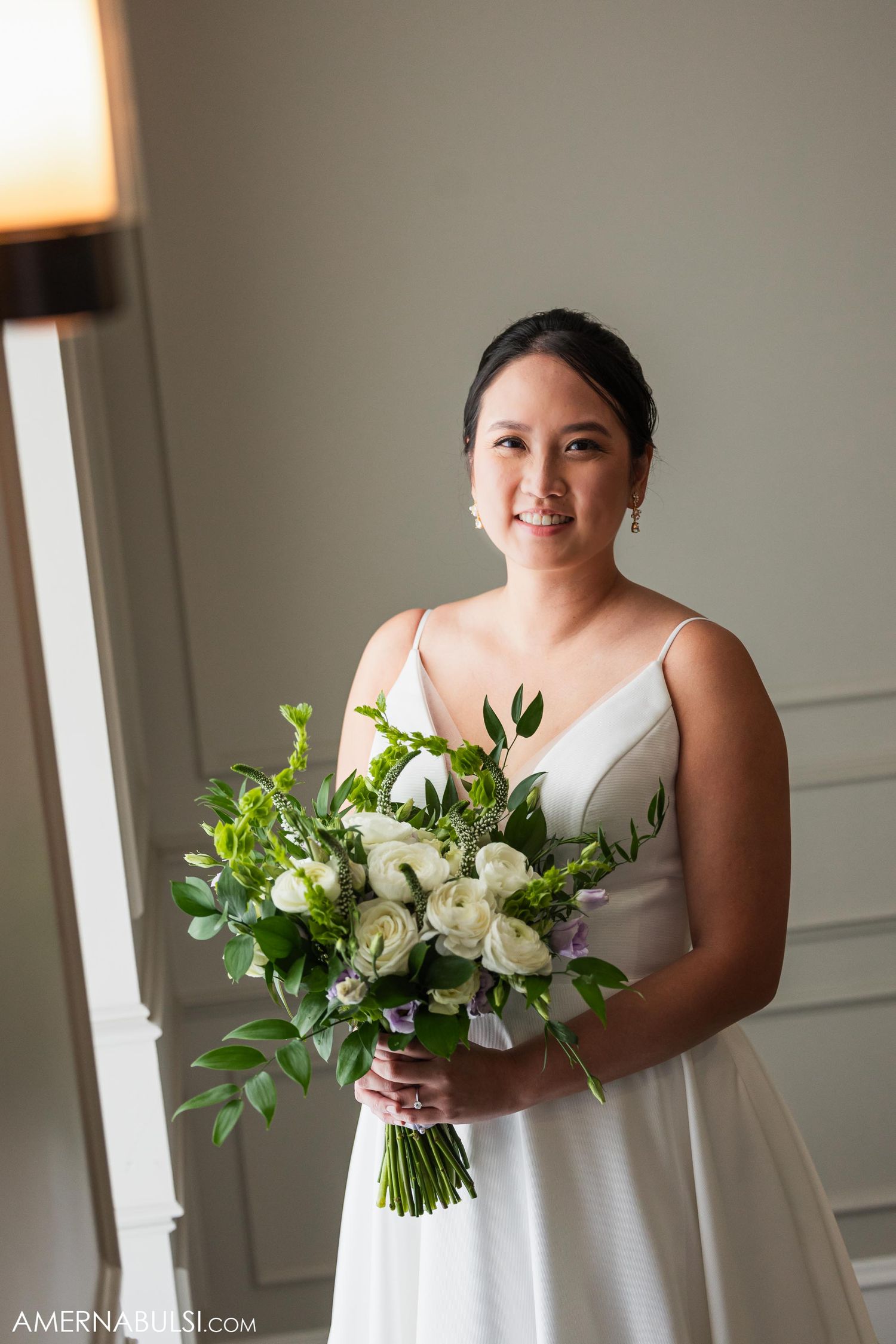 Radiant bride poses with natural white and green wedding bouquet in elegant setting.
