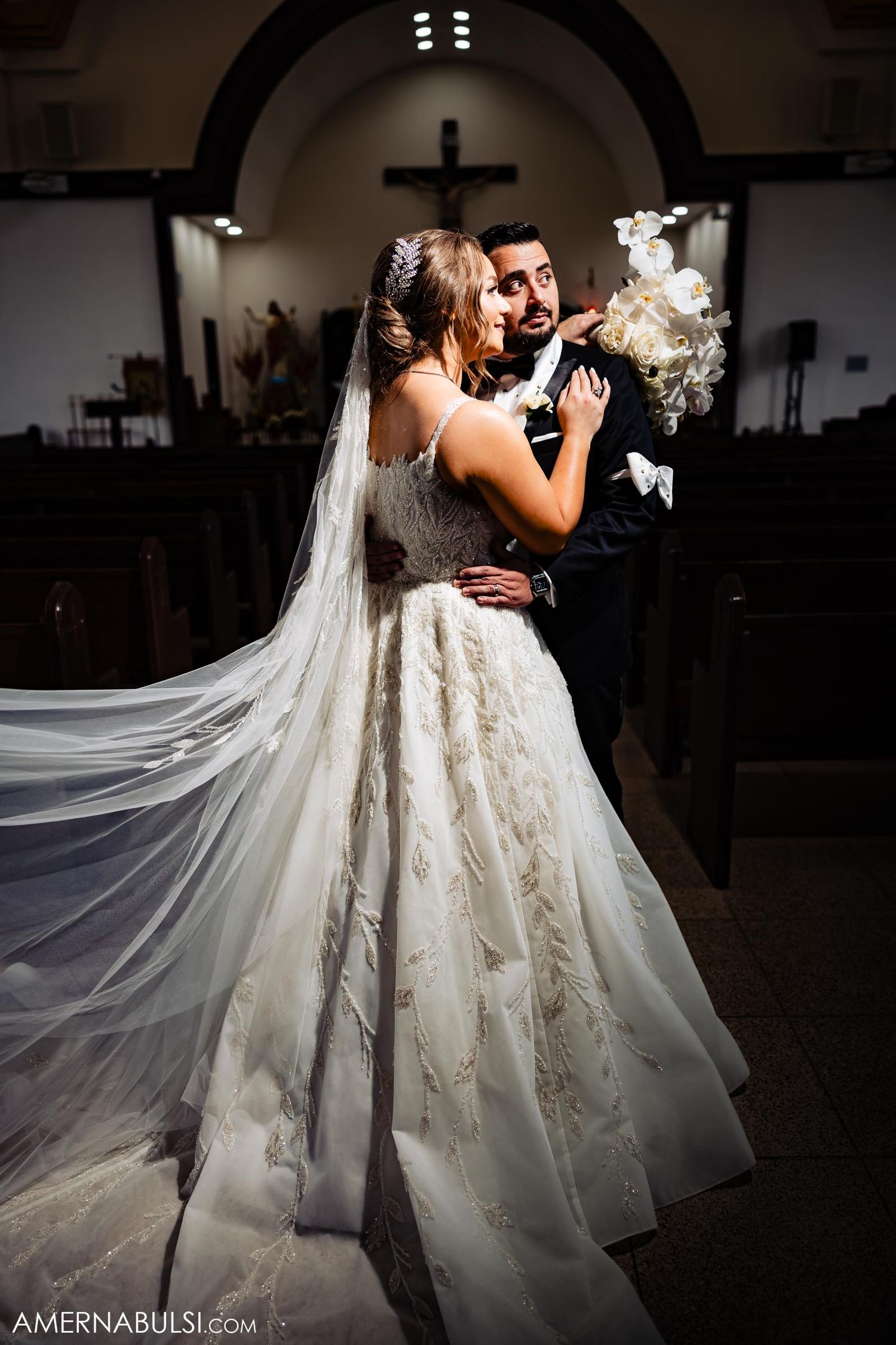 A dramatic church wedding photo with flowing veil and ornate lace dress details.