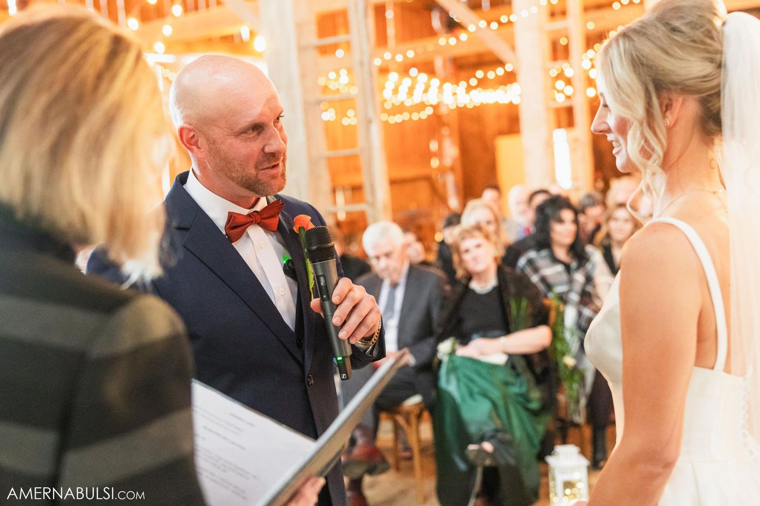 Intimate wedding ceremony moment with string lights glowing in rustic barn setting.