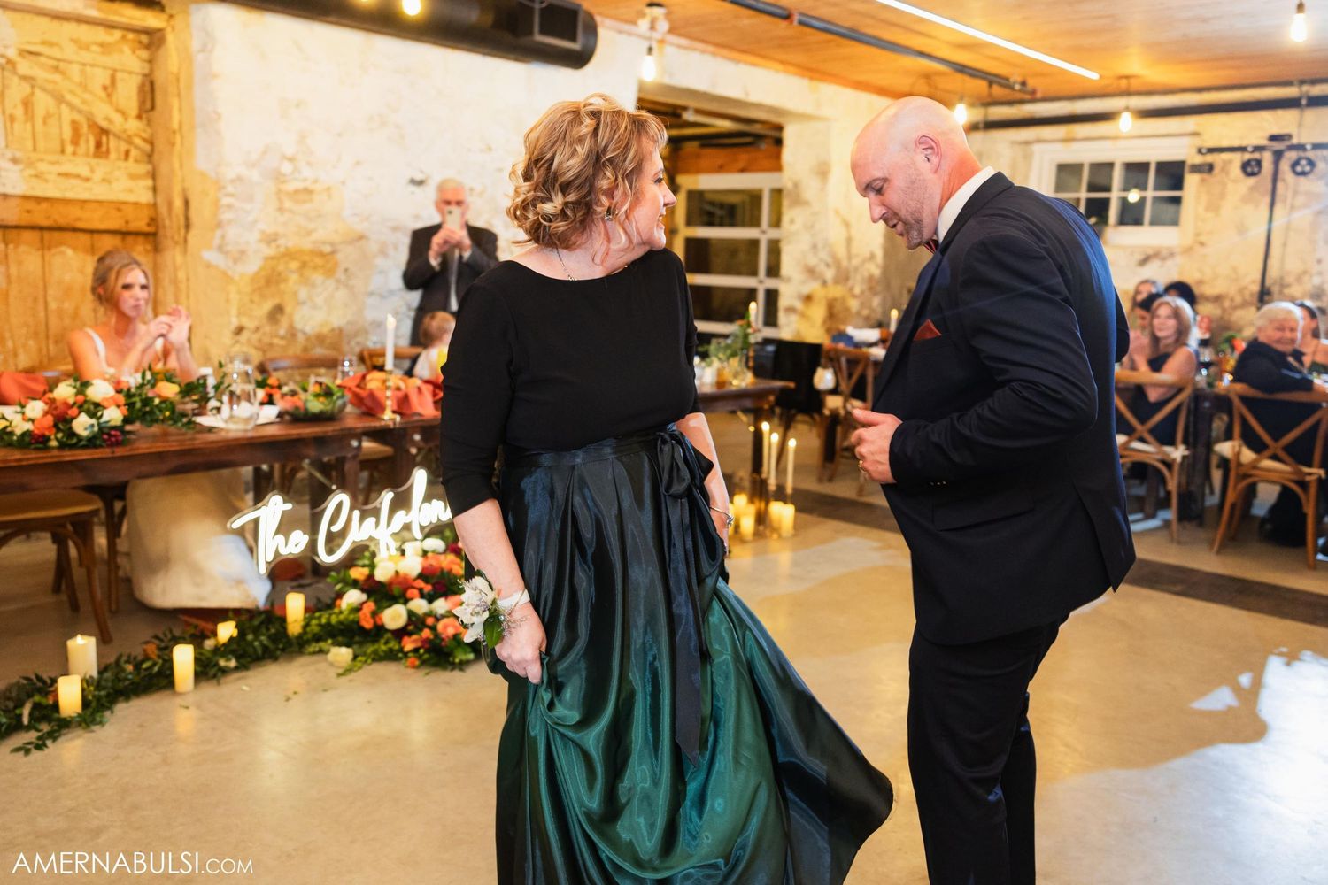 Two people dancing at an elegant event in a rustic venue with string lights.