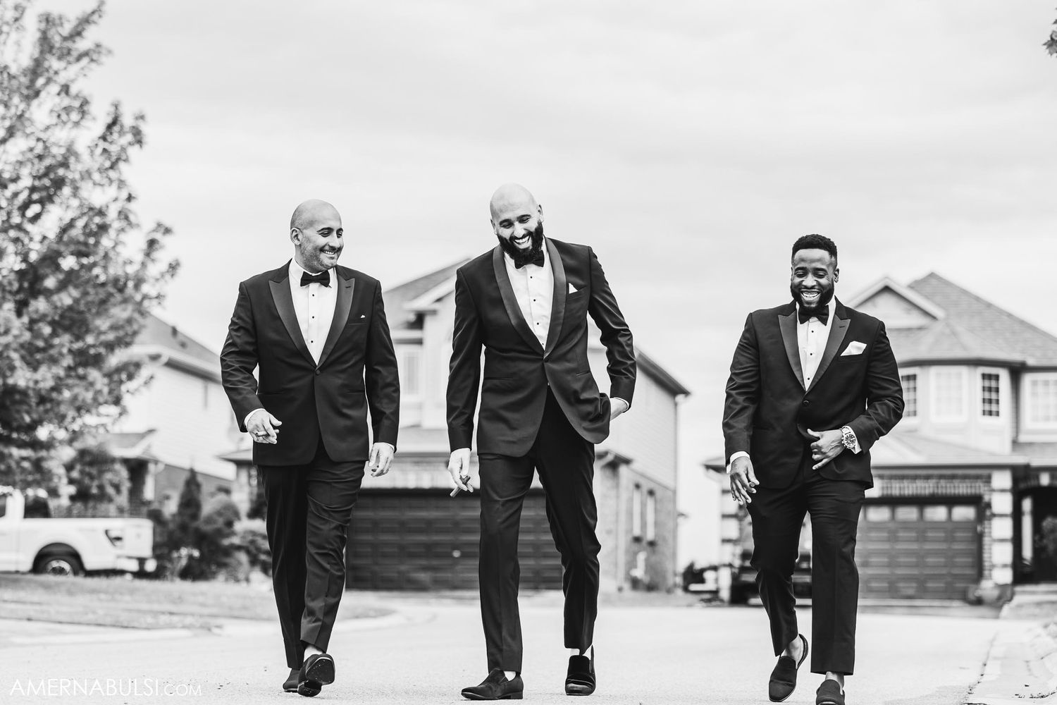 Three people in tuxedos walking together on suburban street.
