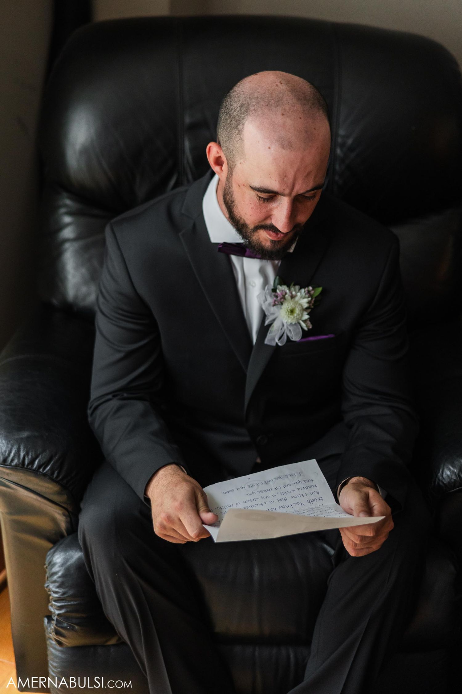 Person in formal black suit reading letter while seated in leather chair.