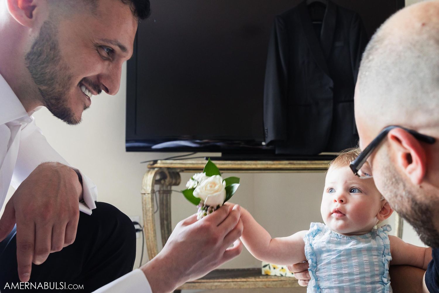 Family member shows flower to smiling baby during intimate moment indoors.