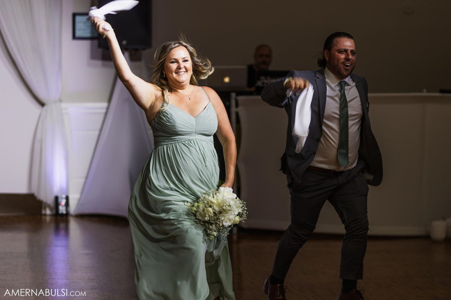 Attendees in formal attire dance enthusiastically while holding a bouquet during reception.